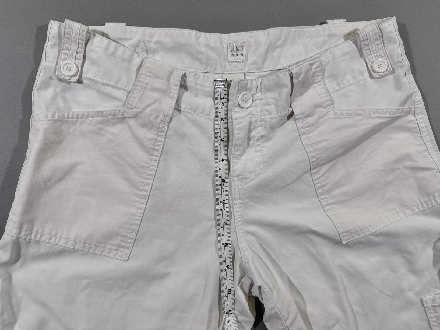 Front rise measurement detail of vintage Abercrombie & Fitch white cargo pants with low-rise waist and utility pocket construction.