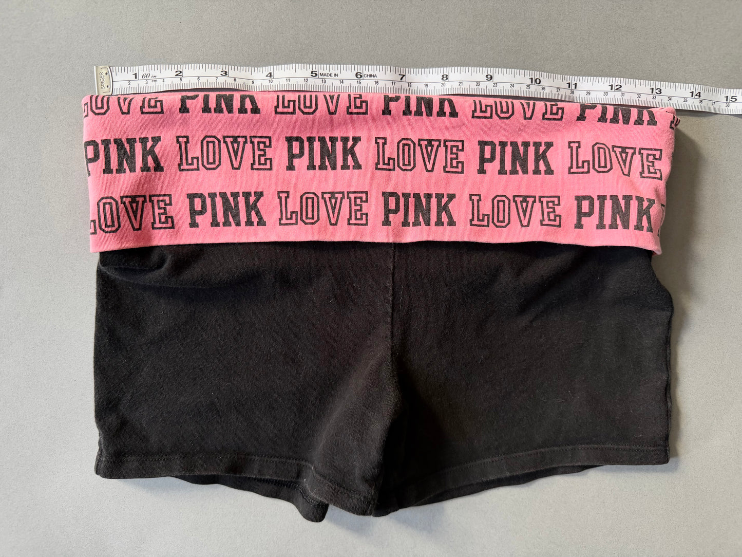 Photo of y2k Victoria’s Secret PINK yoga shorts with pink foldover waistband and measuring tape showing 26 inches waist