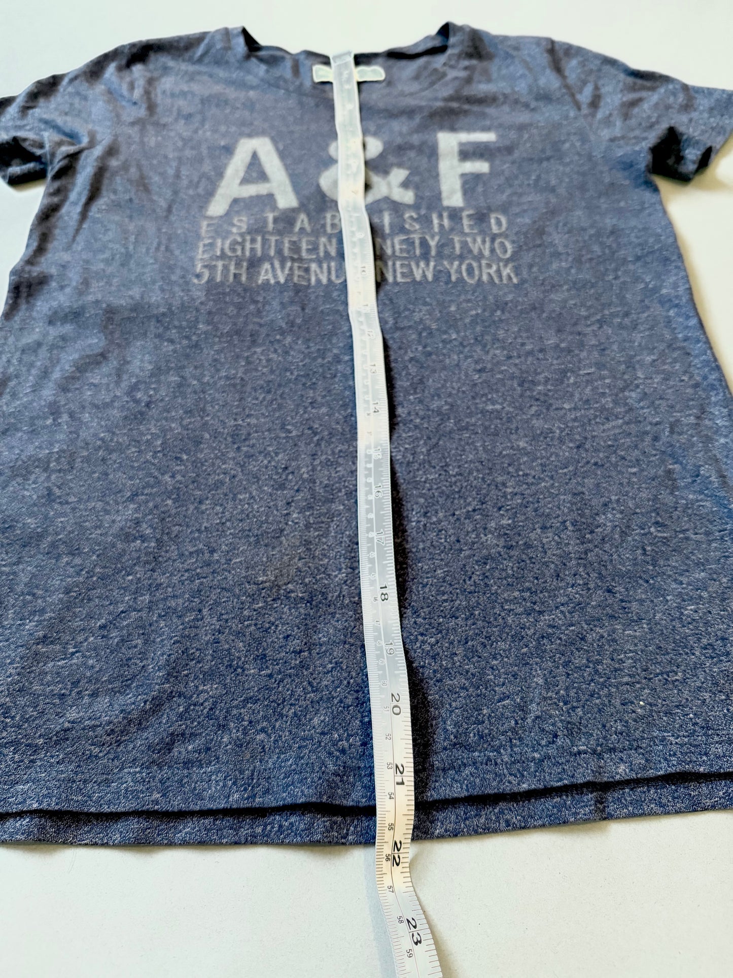 Navy blue Abercrombie & fitch t-shirt with 'A&F' logo against fabric measuring tape showing length