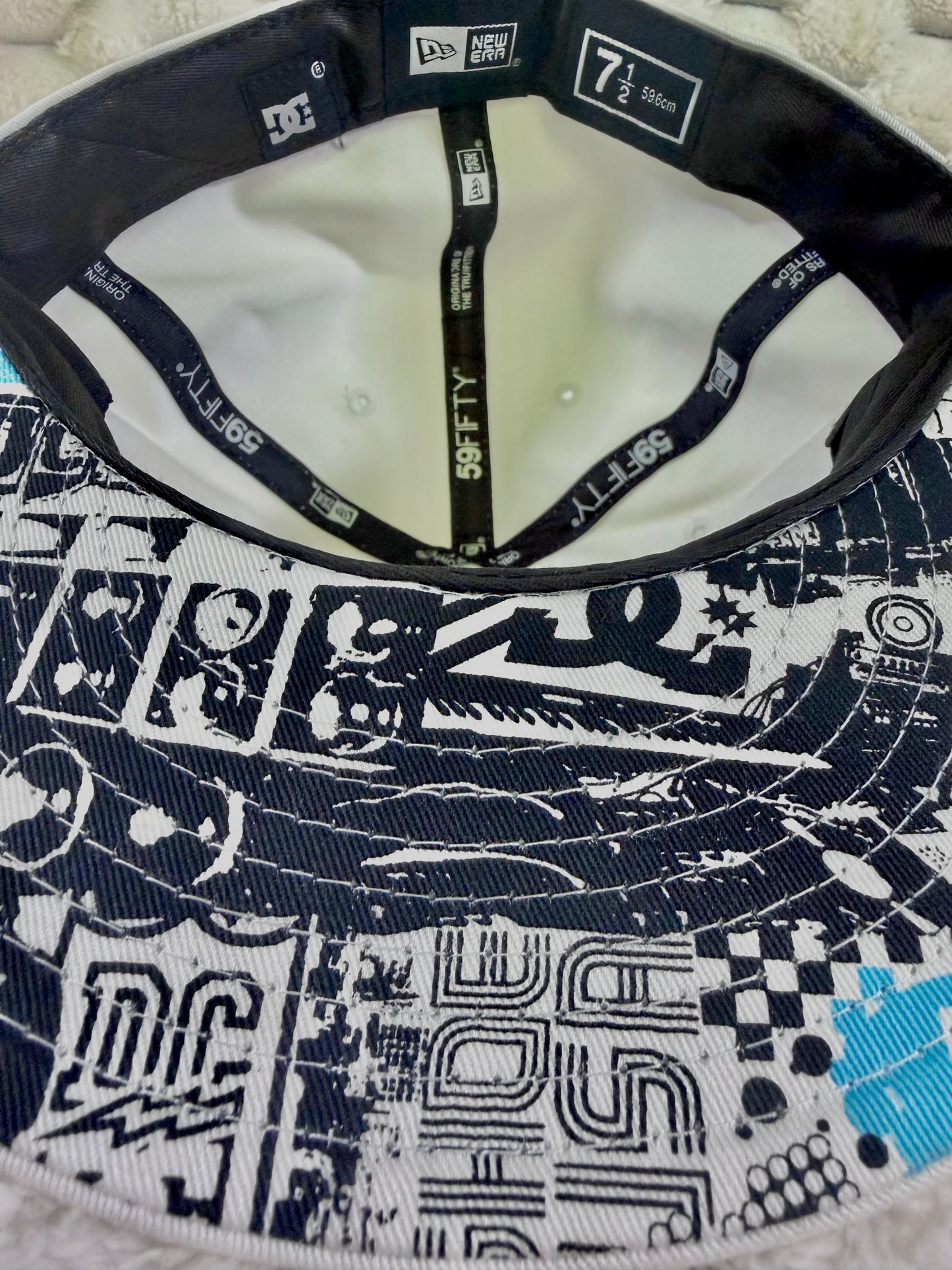 Close-up of DC Shoes New Era fitted cap interior showing size 7 1/2 label, branded sweatband and graphic-print underside of flat brim.