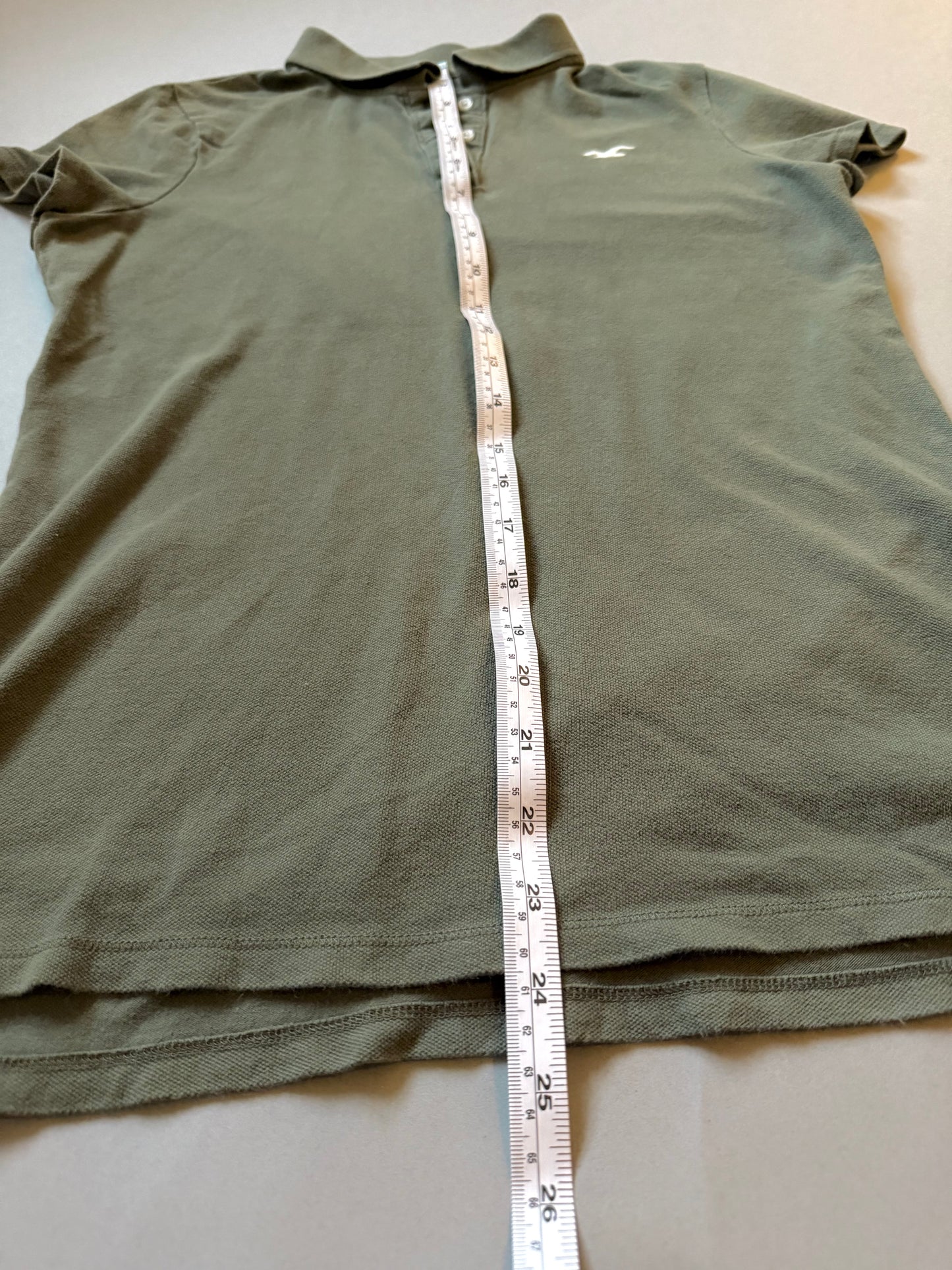 2000s women’s green Hollister polo with measuring tape showing 23 inches length. 