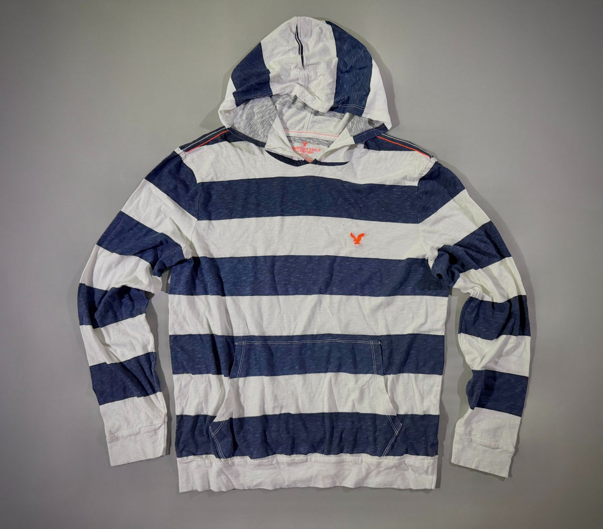 Photo of a long sleeve hooded shirt from American Eagle with thick navy and white stripes and orange eagle embroidery. 