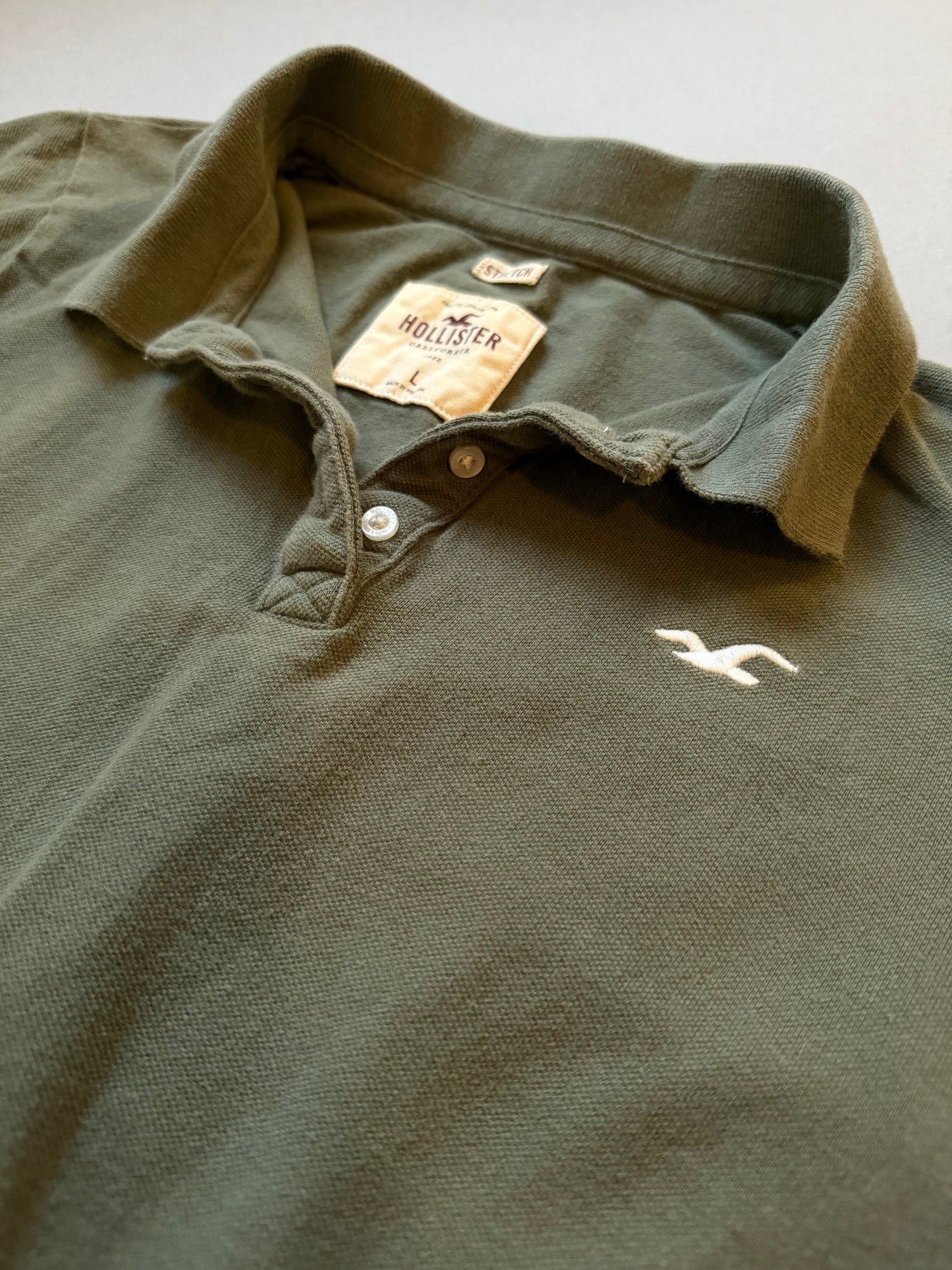 Close up of olive green Hollister polo collar and embroidered branding 