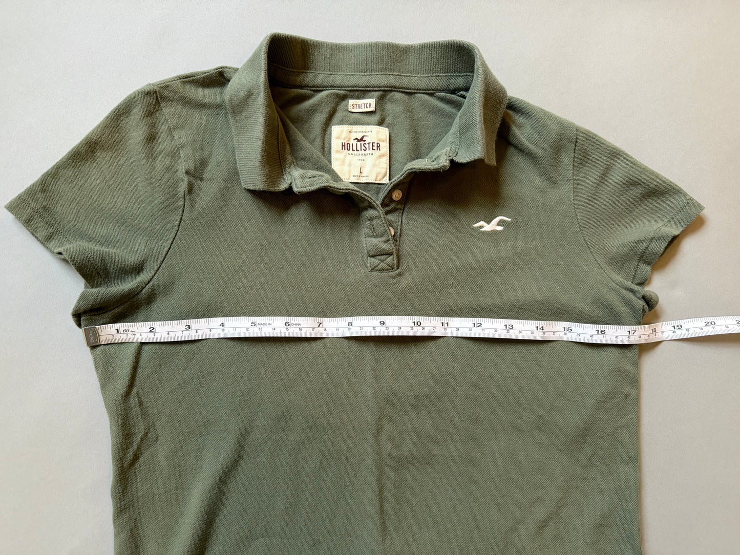 2000s women's green Hollister polo with measuring tape showing 17 inches pit to pit. 