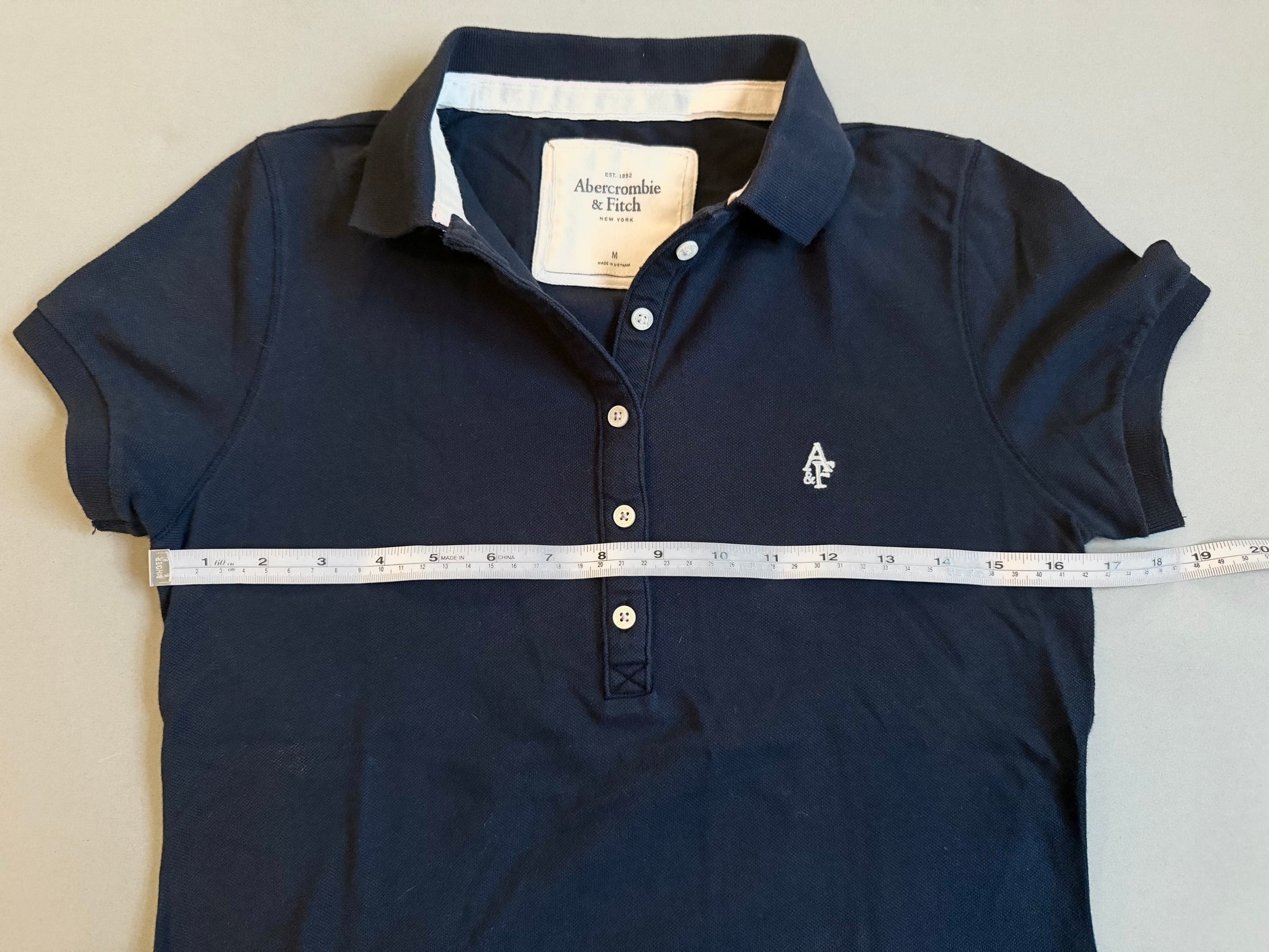 Abercrombje & fitch 2000s women’s navy short sleeve polo shirt with measuring tape showing 16.5 inches pit to pit. 