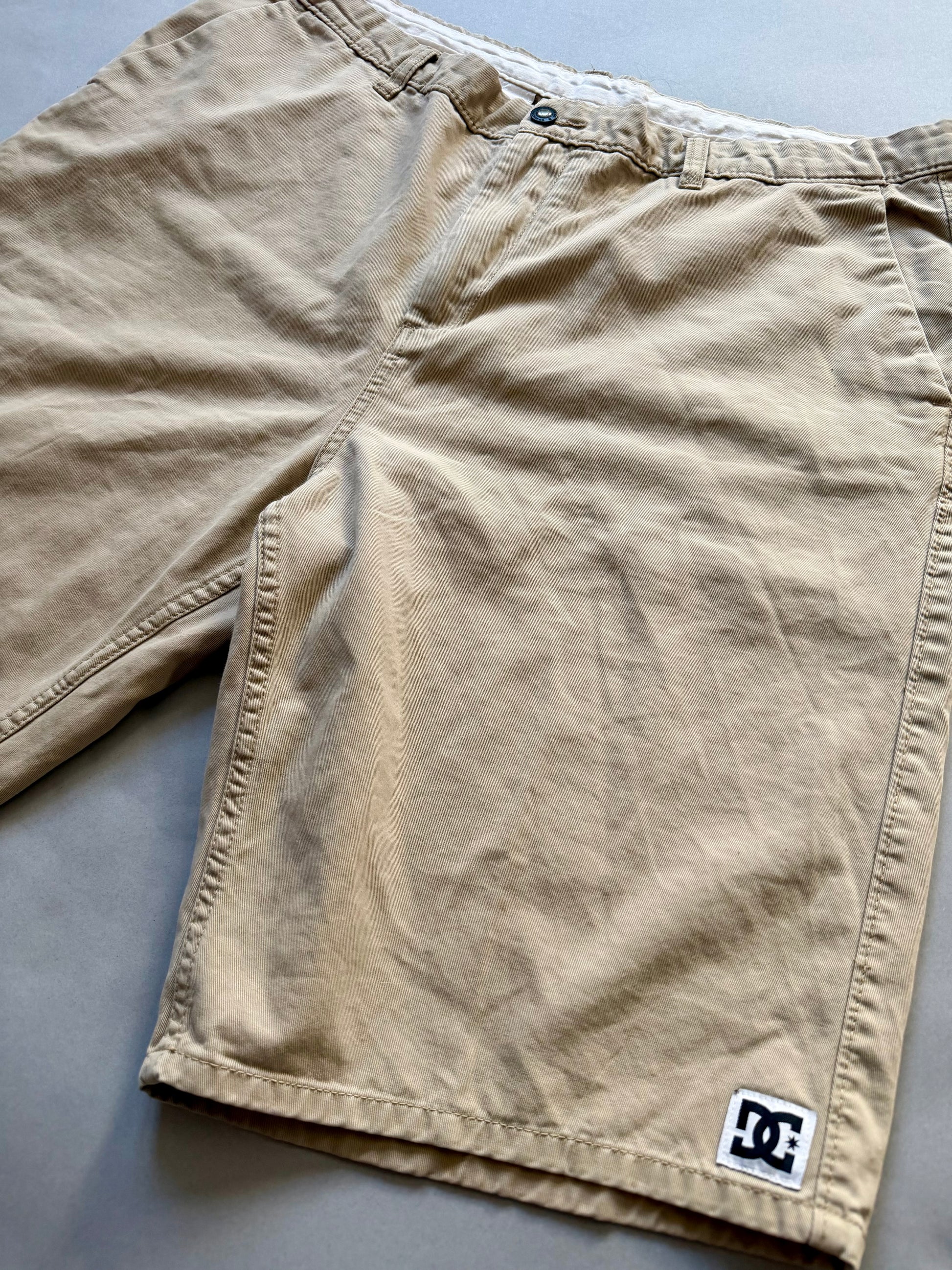 Angled photo of men’s khaki DC skate shorts showing logo patch on bottom right hem 