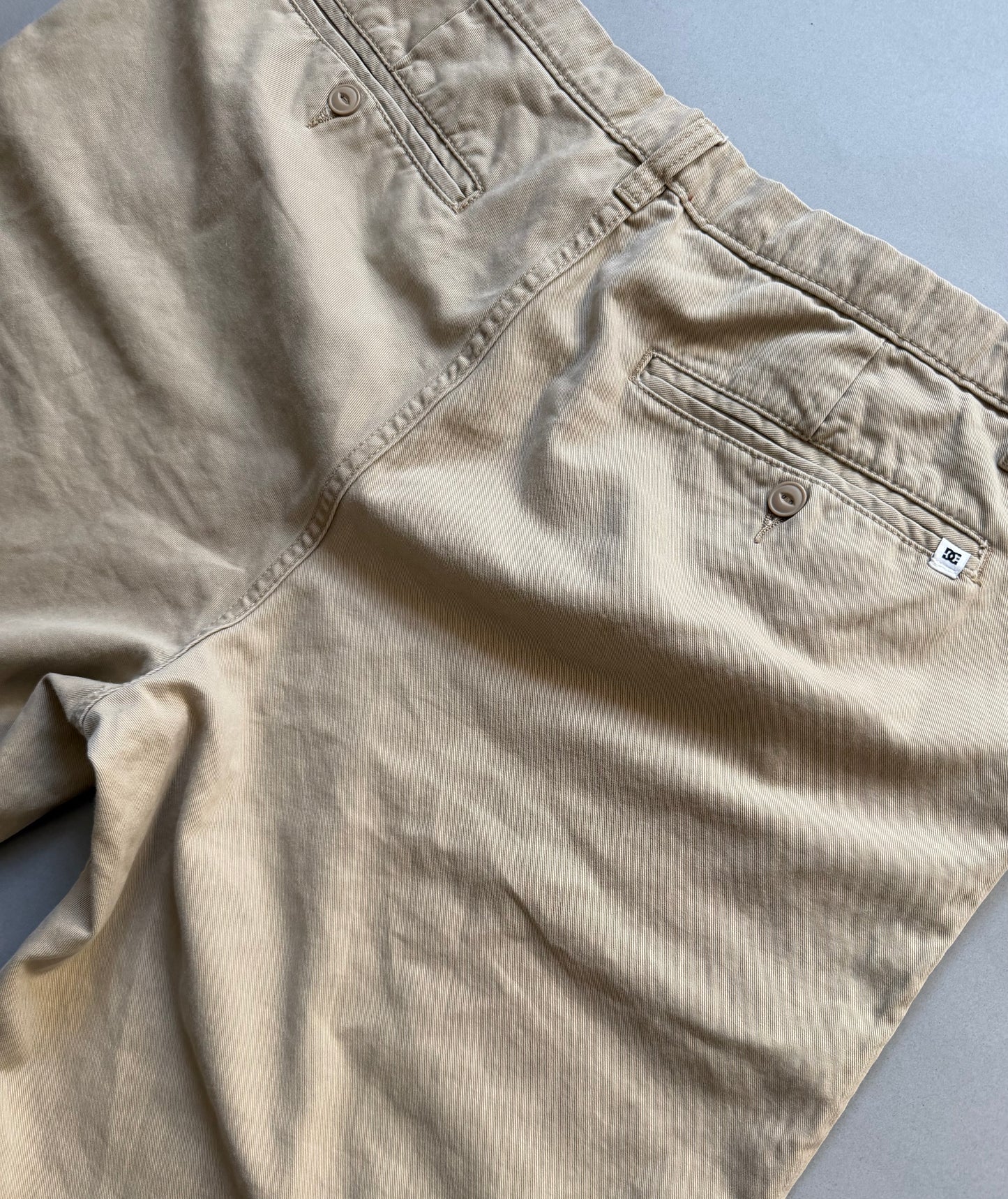 Angled photo of backside of men’s khaki DC chino skate shorts showing tiny logo patch on right pocket 