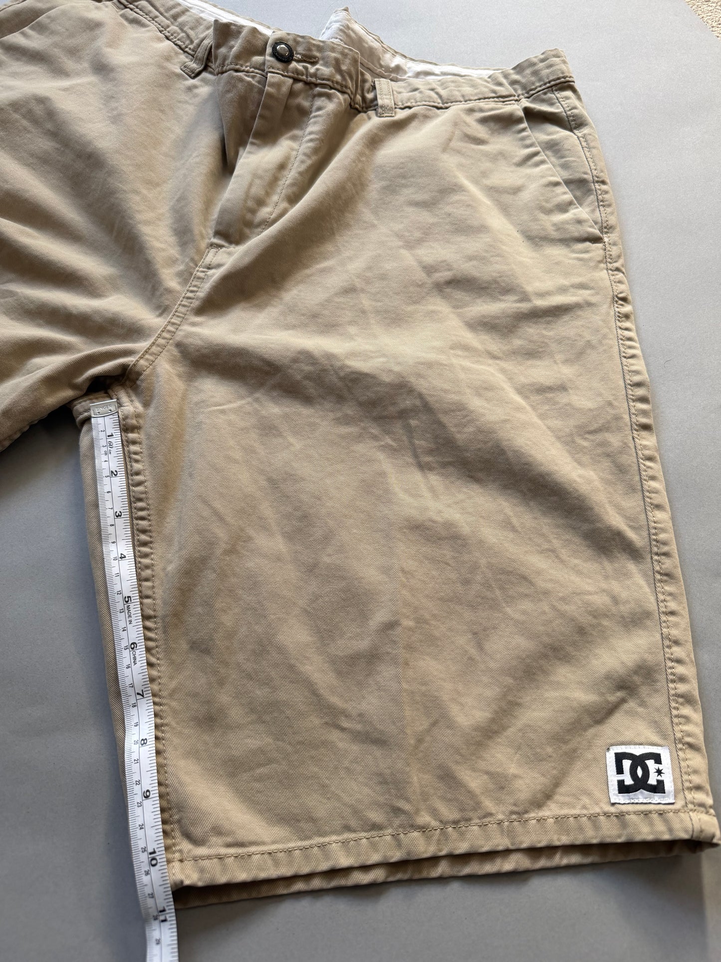 Men’s khaki DC chino skate shorts with measuring tape showing inseam measurement 10.5 inches 