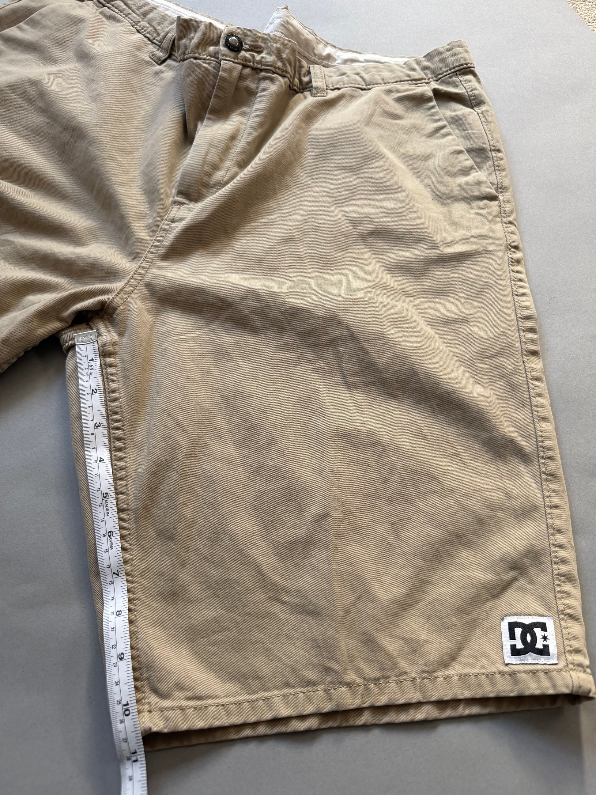 Men’s khaki DC chino skate shorts with measuring tape showing inseam measurement 10.5 inches 