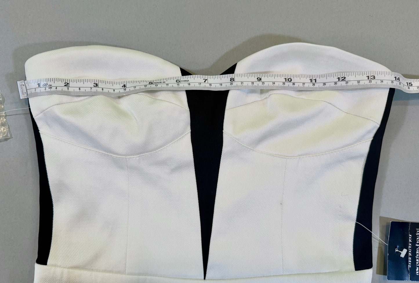 Close up of Bebe mini dress with strapless corset style top and measuring tape showing 14 inches pit to pit 