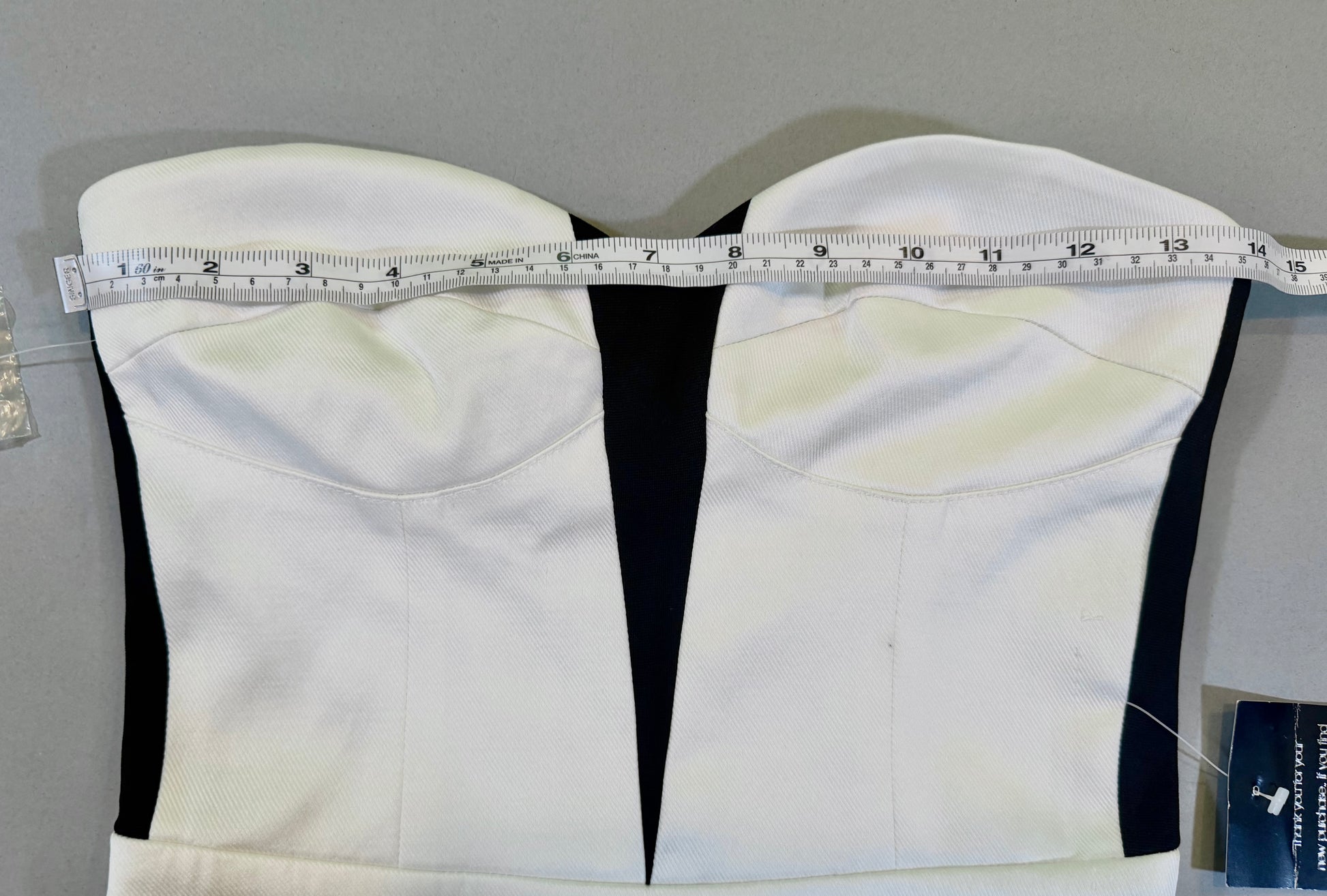 Close up of Bebe mini dress with strapless corset style top and measuring tape showing 14 inches pit to pit 