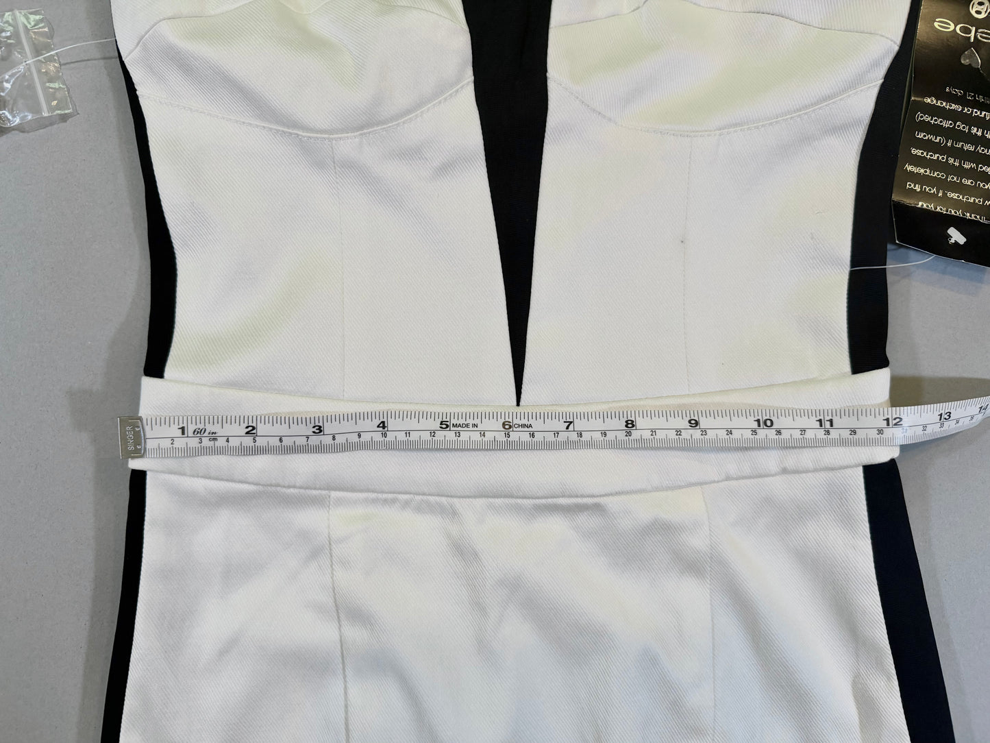 Close up of black and white Bebe cocktail dress with measuring tape showing 12 inches waist 