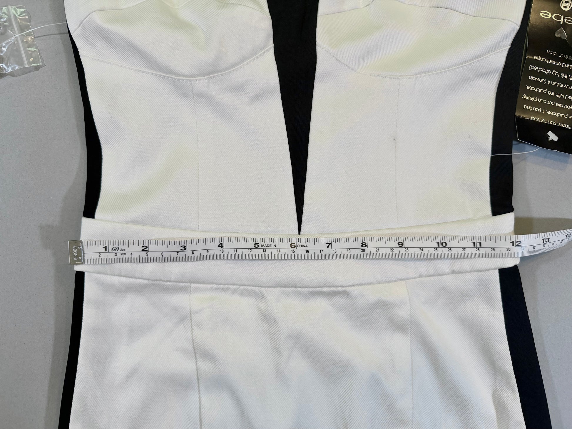 Close up of black and white Bebe cocktail dress with measuring tape showing 12 inches waist 