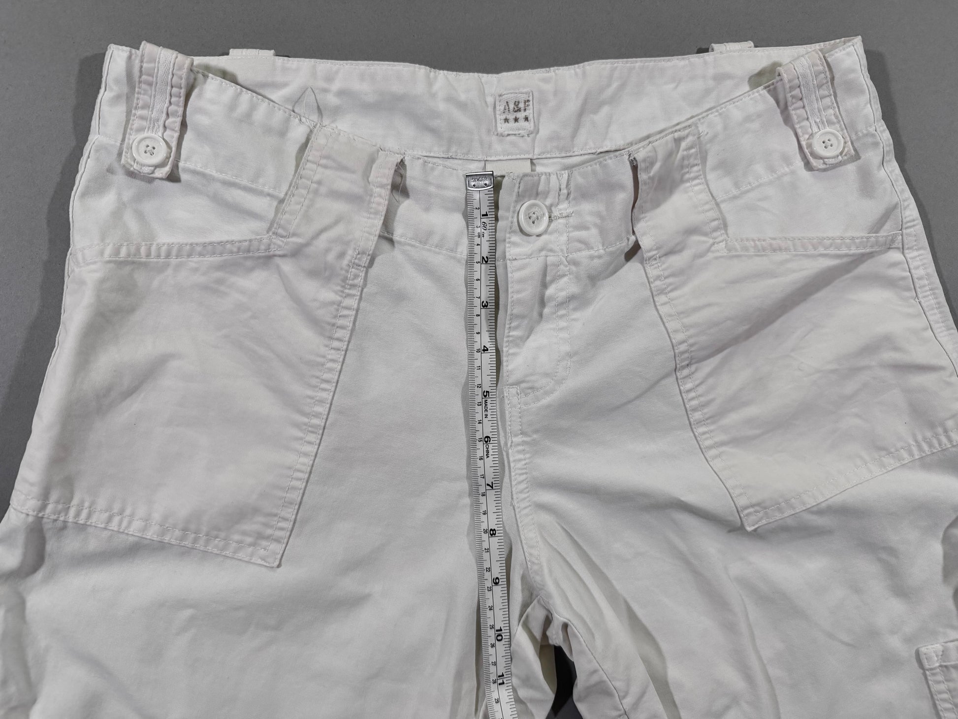 Front rise measurement detail of vintage Abercrombie & Fitch white cargo pants with low-rise waist and utility pocket construction.