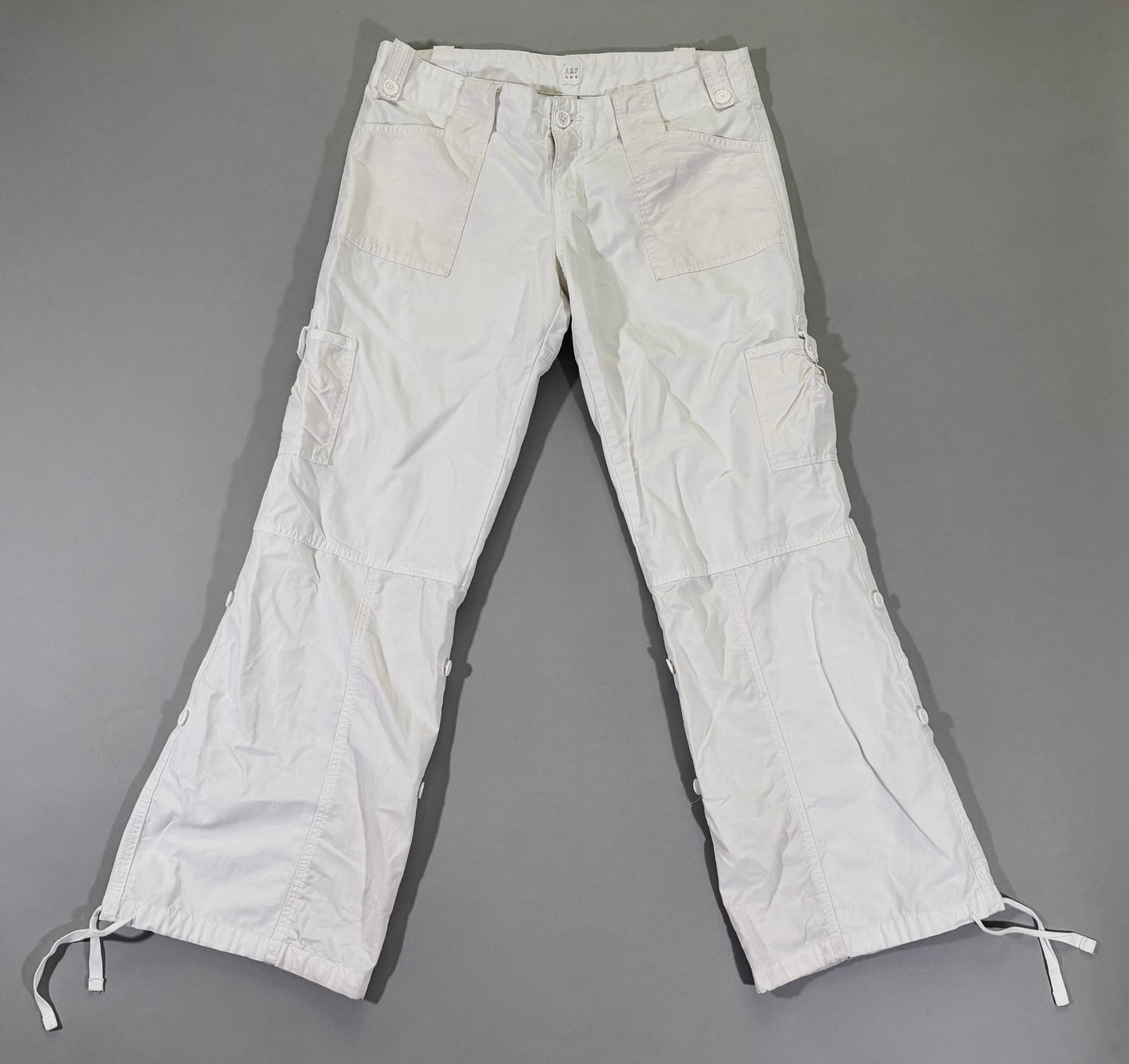 Vintage Y2K Abercrombie & Fitch white wide-leg cargo pants with utility pockets, button-tab details, and adjustable drawstring hems, front view.