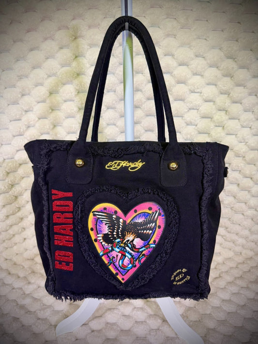 Front view of Y2K Ed Hardy Christian Audigier black canvas tote bag with eagle heart graphic, rhinestone logo and gold hardware.