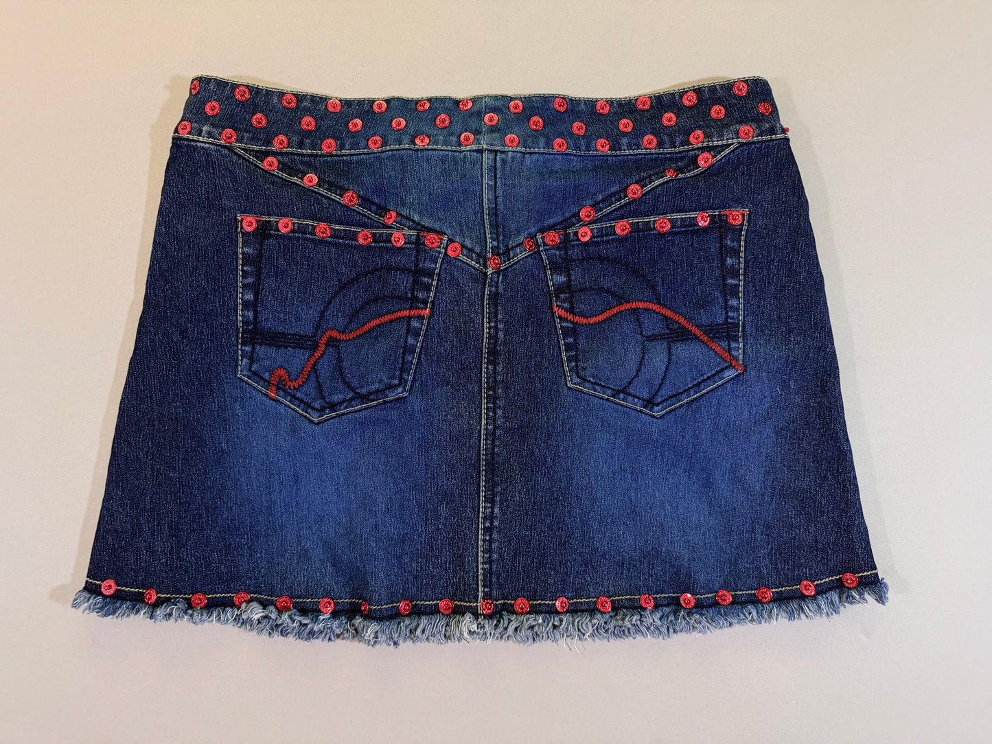 Back view of vintage denim mini skirt showing red rivets in curving V design and embroidered pockets 