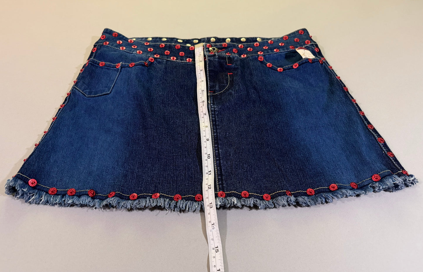 Photo of 2000s denim mini skirt with measuring tape showing 13 inches length 