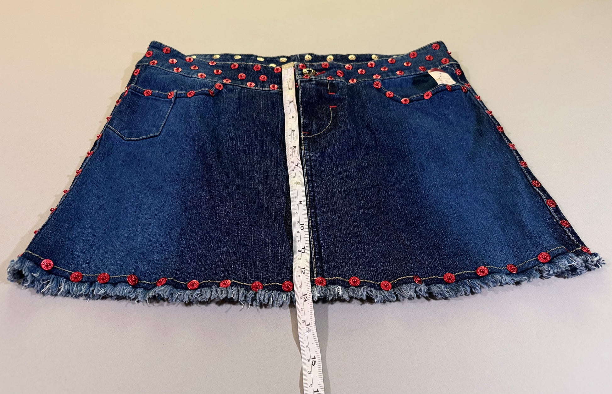 Photo of 2000s denim mini skirt with measuring tape showing 13 inches length 