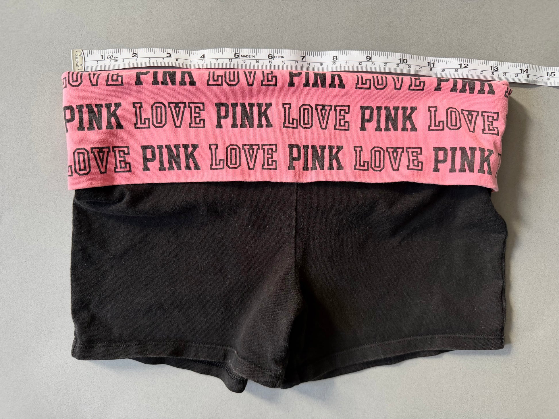 Photo of y2k Victoria’s Secret PINK yoga shorts with pink foldover waistband and measuring tape showing 26 inches waist 
