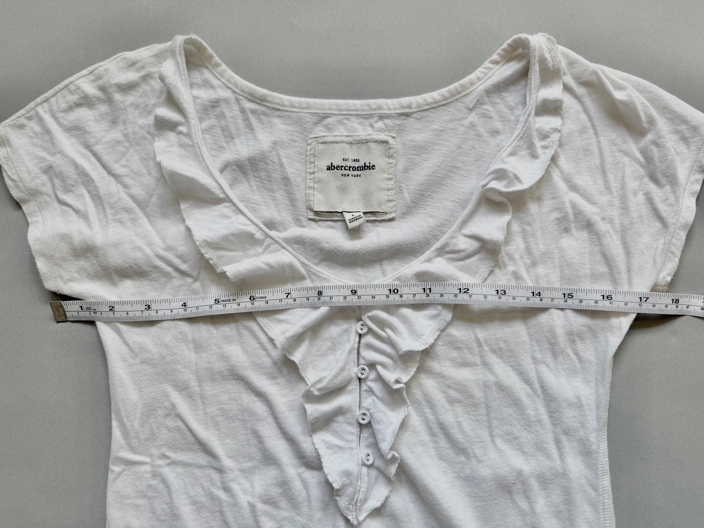 White Abercrombie & fitch ruffle top with measuring tape showing pit to pit length. 