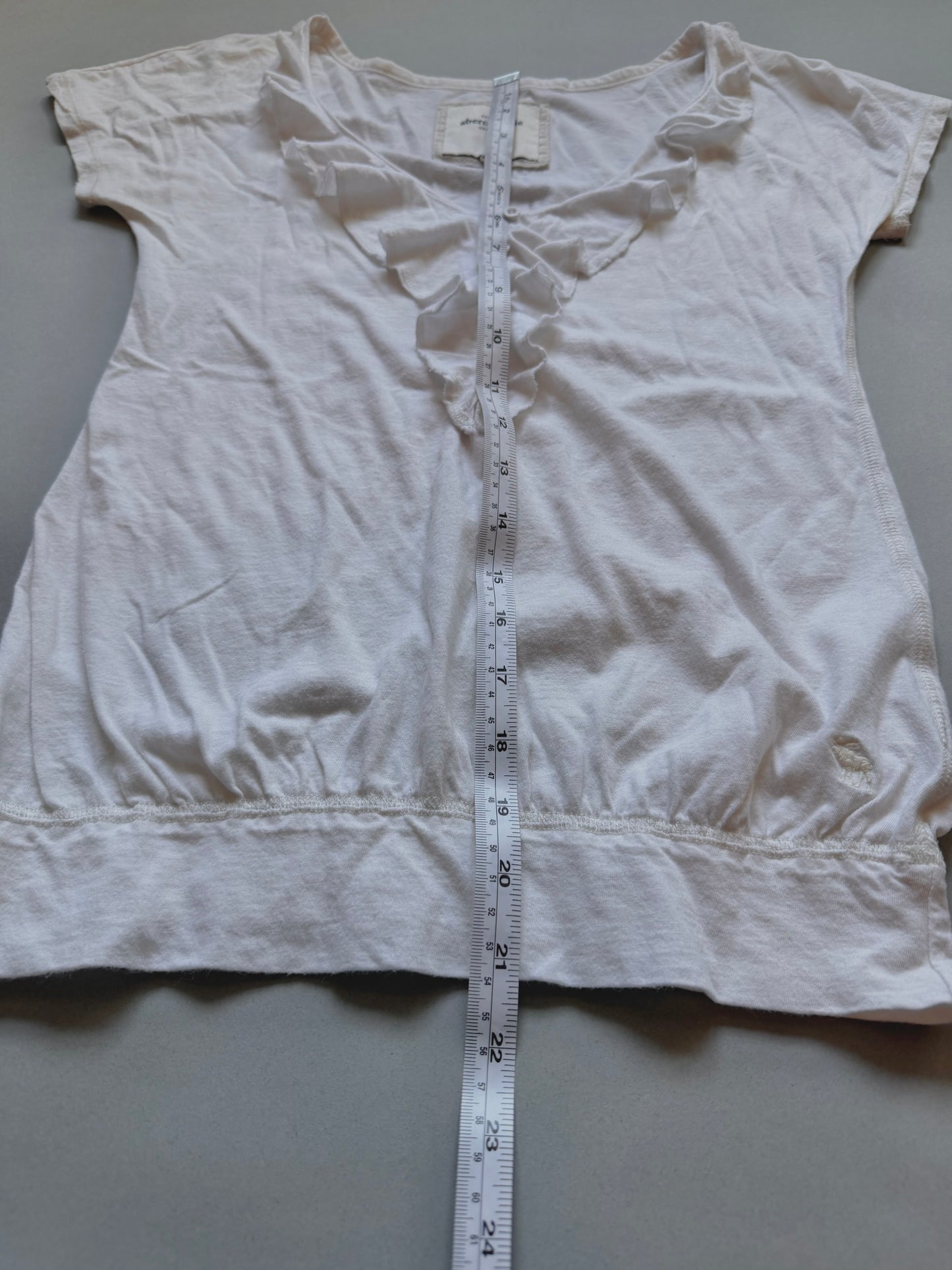 White Abercrombie & fitch ruffle top with measuring tape showing length from top to bottom. 