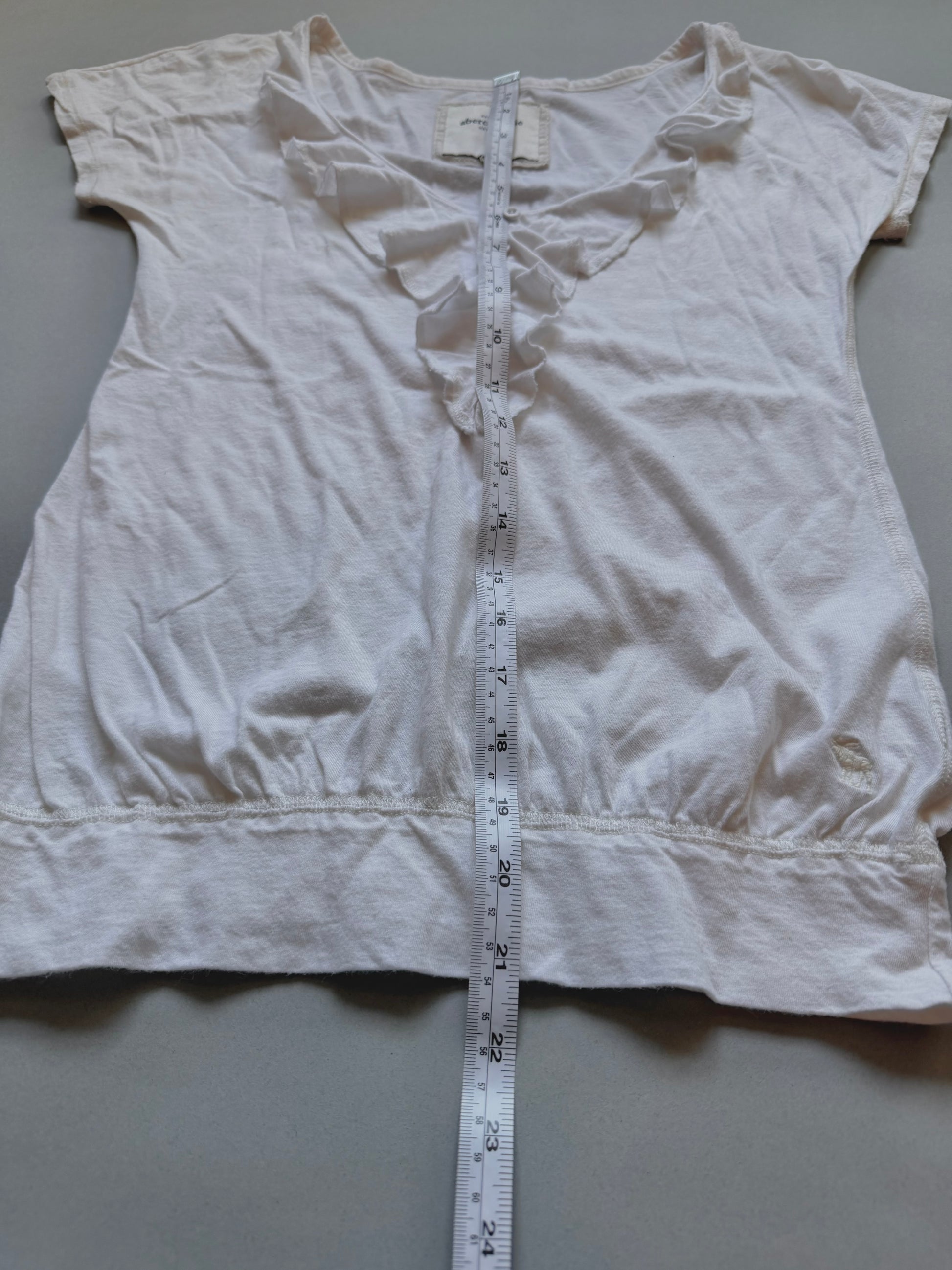 White Abercrombie & fitch ruffle top with measuring tape showing length from top to bottom. 