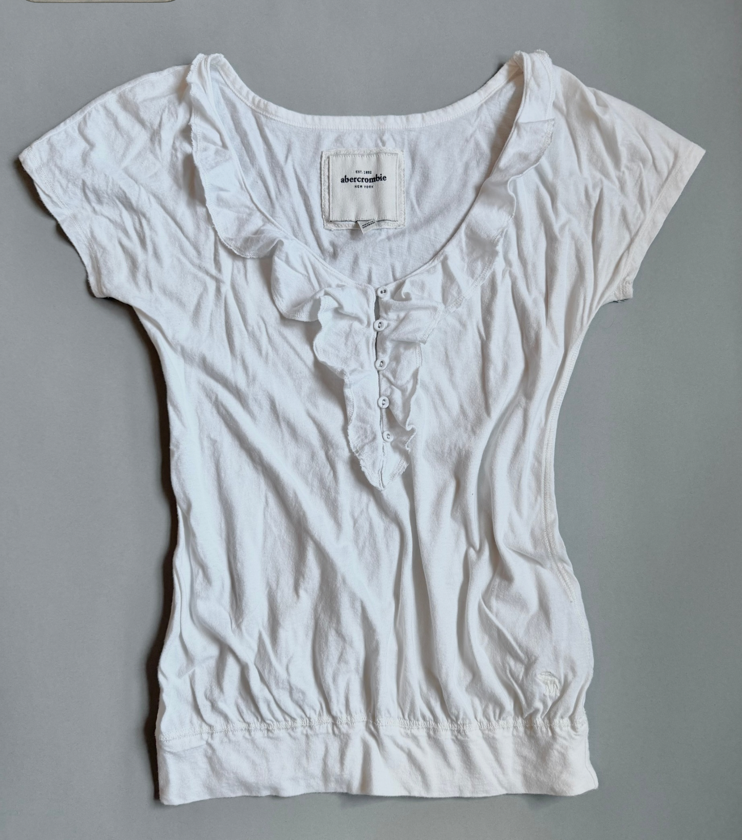 White Abercrombie & Fitch ruffle top with bubble silhouette against grey backdrop 
