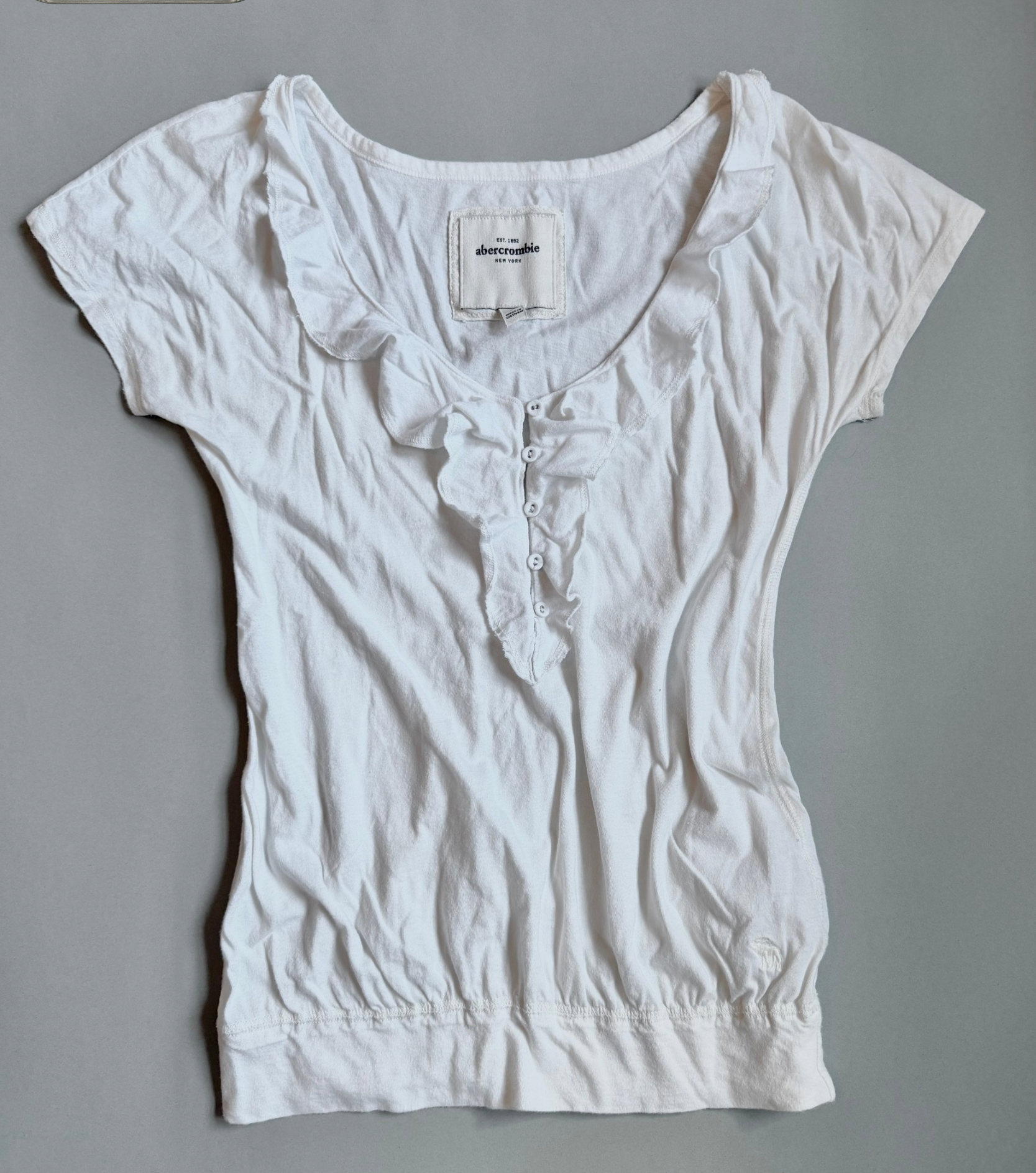 White Abercrombie & Fitch ruffle top with bubble silhouette against grey backdrop 