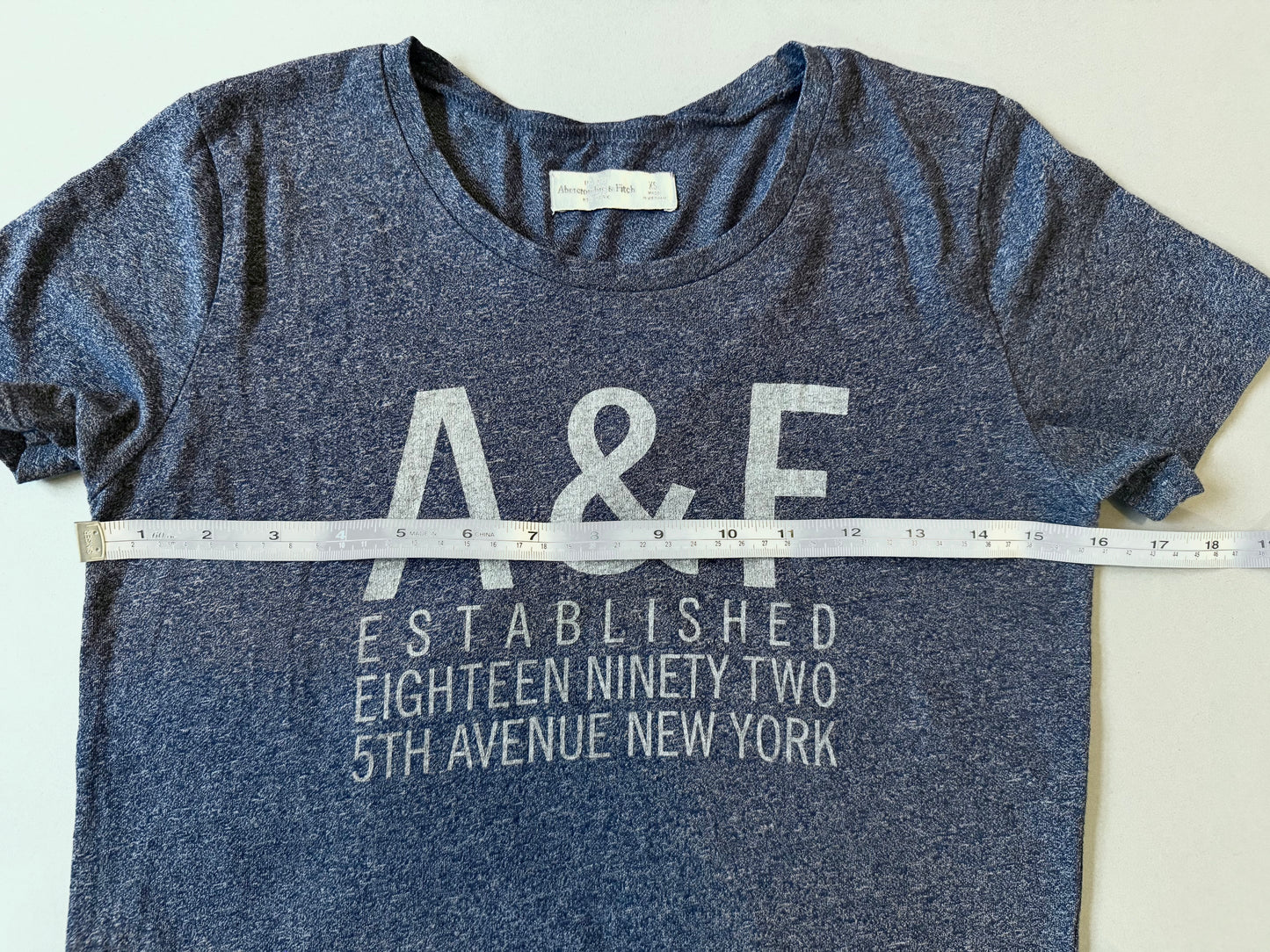 Navy blue Abercrombie & Fitch t-shirt with 'A&F' logo and text, measured pit to pit against fabric measuring tape.