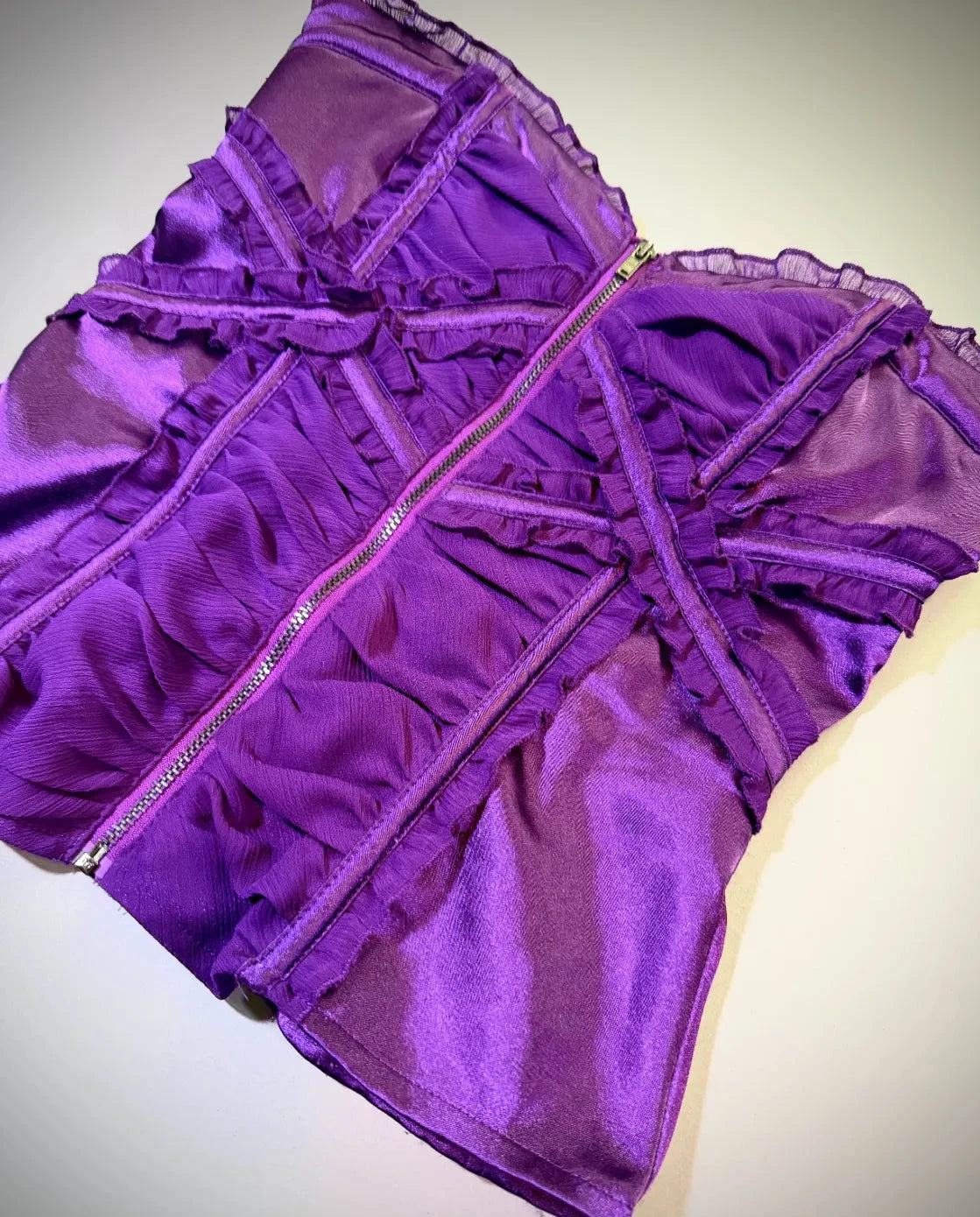 Angled photo of purple satin corset top from Bebe with chiffon ruffles and metal zipper down middle 