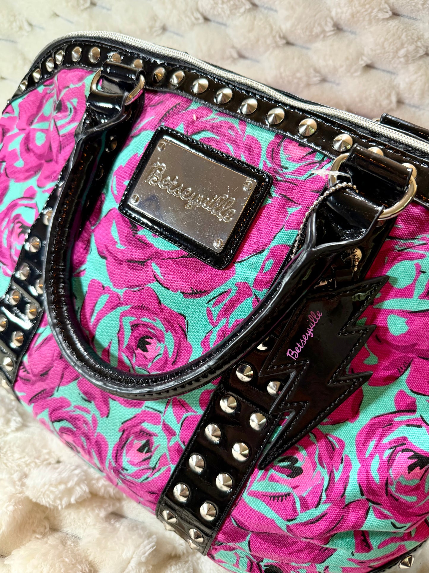 Close-up of the Betseyville logo plaque, black patent handles, silver stud accents, and signature lightning bolt charm.