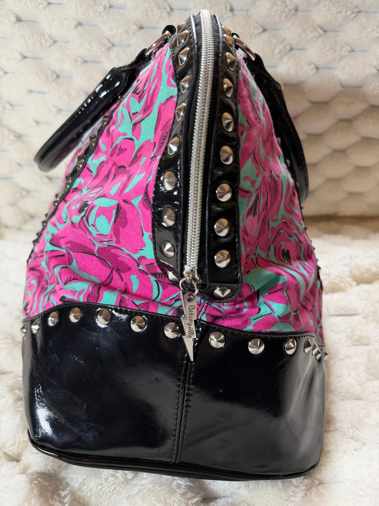 Side profile of the Betseyville floral duffel bag showing the structured silhouette, studded trim, and zip-top closure.