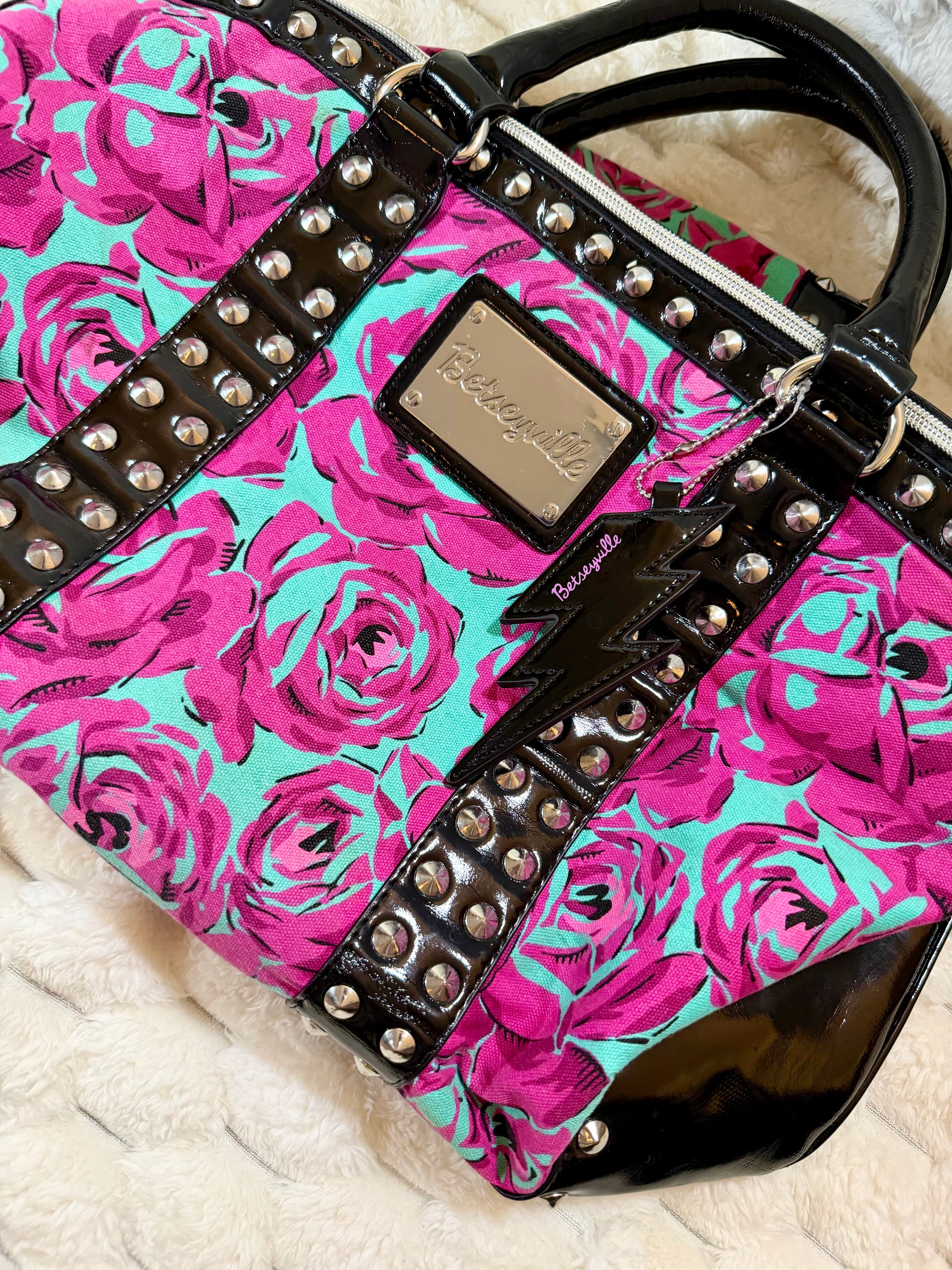 Angled view highlighting the bold floral print, glossy patent trim, silver studs, and Betseyville logo hardware.