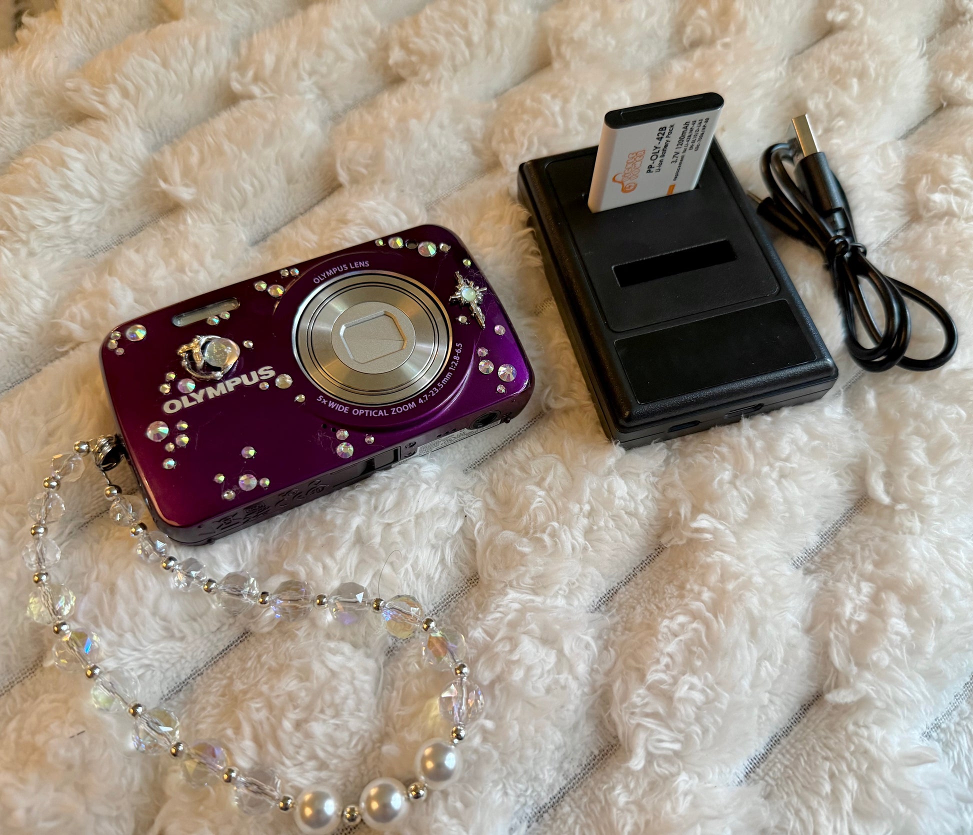 Purple Olympus digital camera decorated with rhinestones and celestial charms, with battery charger 
