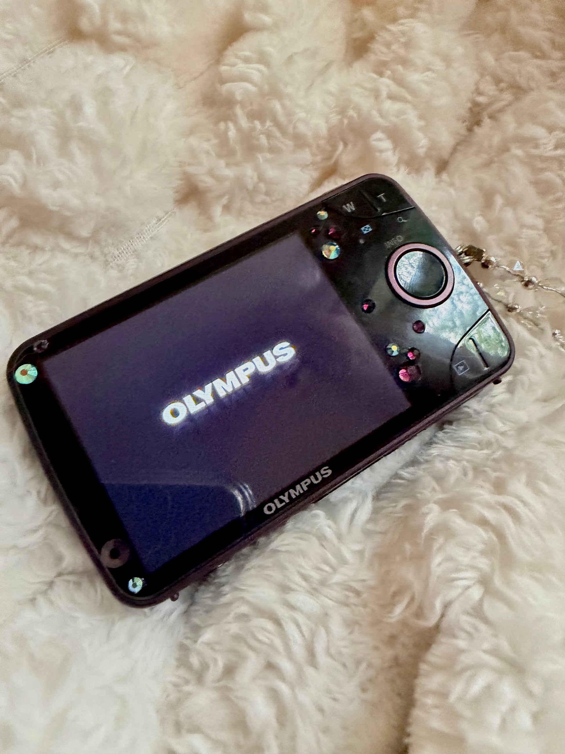 Back of purple Olympus digital camera showing LCD screen on with Olympus logo