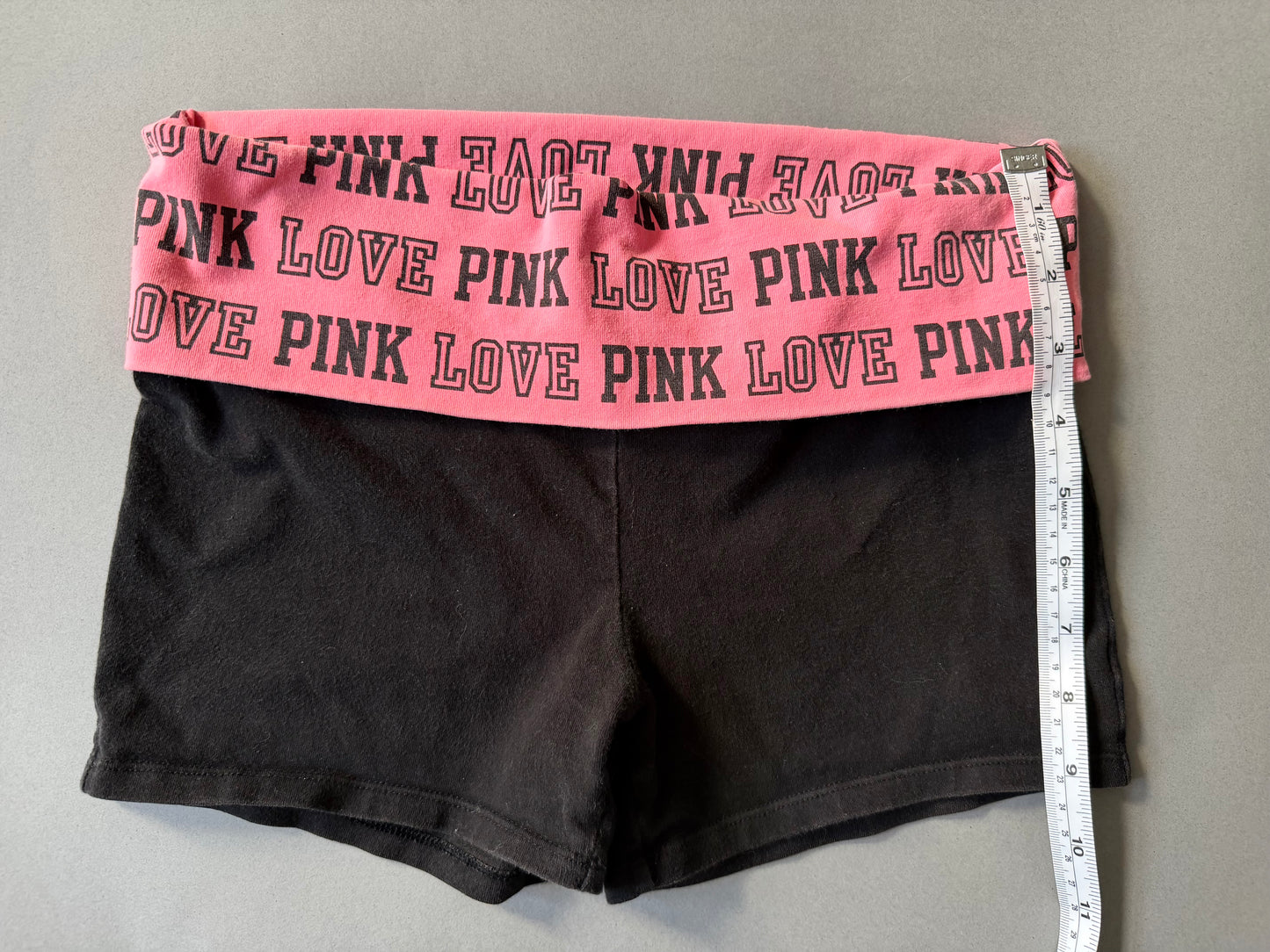 Photo of y2k Victoria’s Secret PINK yoga shorts with pink foldover waistband and a measuring tape showing 9 inches leg length 