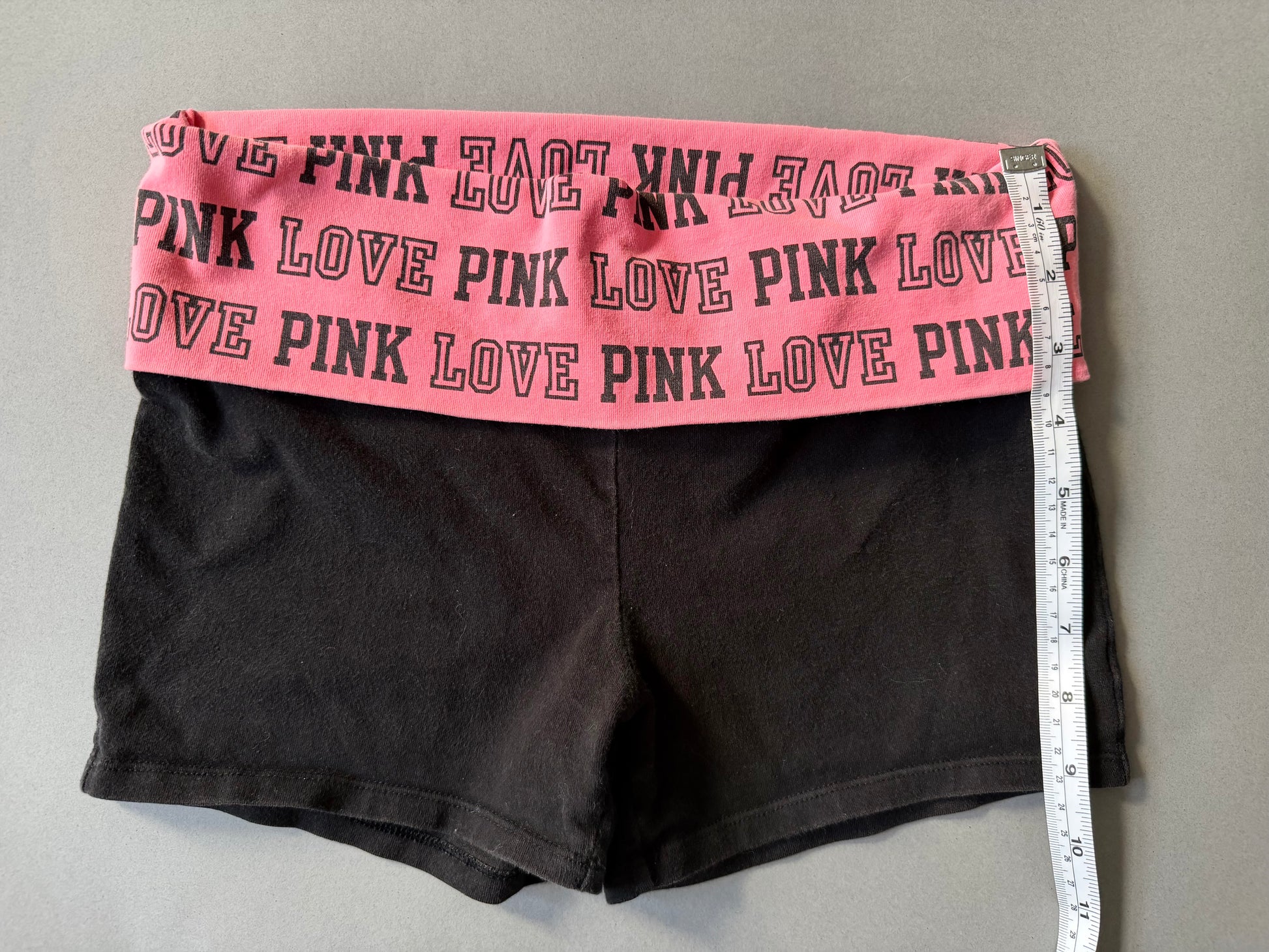 Photo of y2k Victoria’s Secret PINK yoga shorts with pink foldover waistband and a measuring tape showing 9 inches leg length 