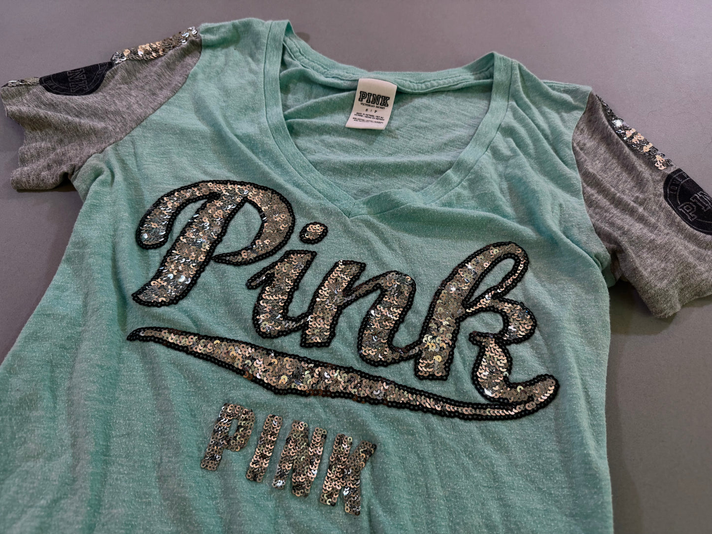 Close-up of the silver sequin PINK logo on an aqua blue green Victoria’s Secret PINK V-neck tee.