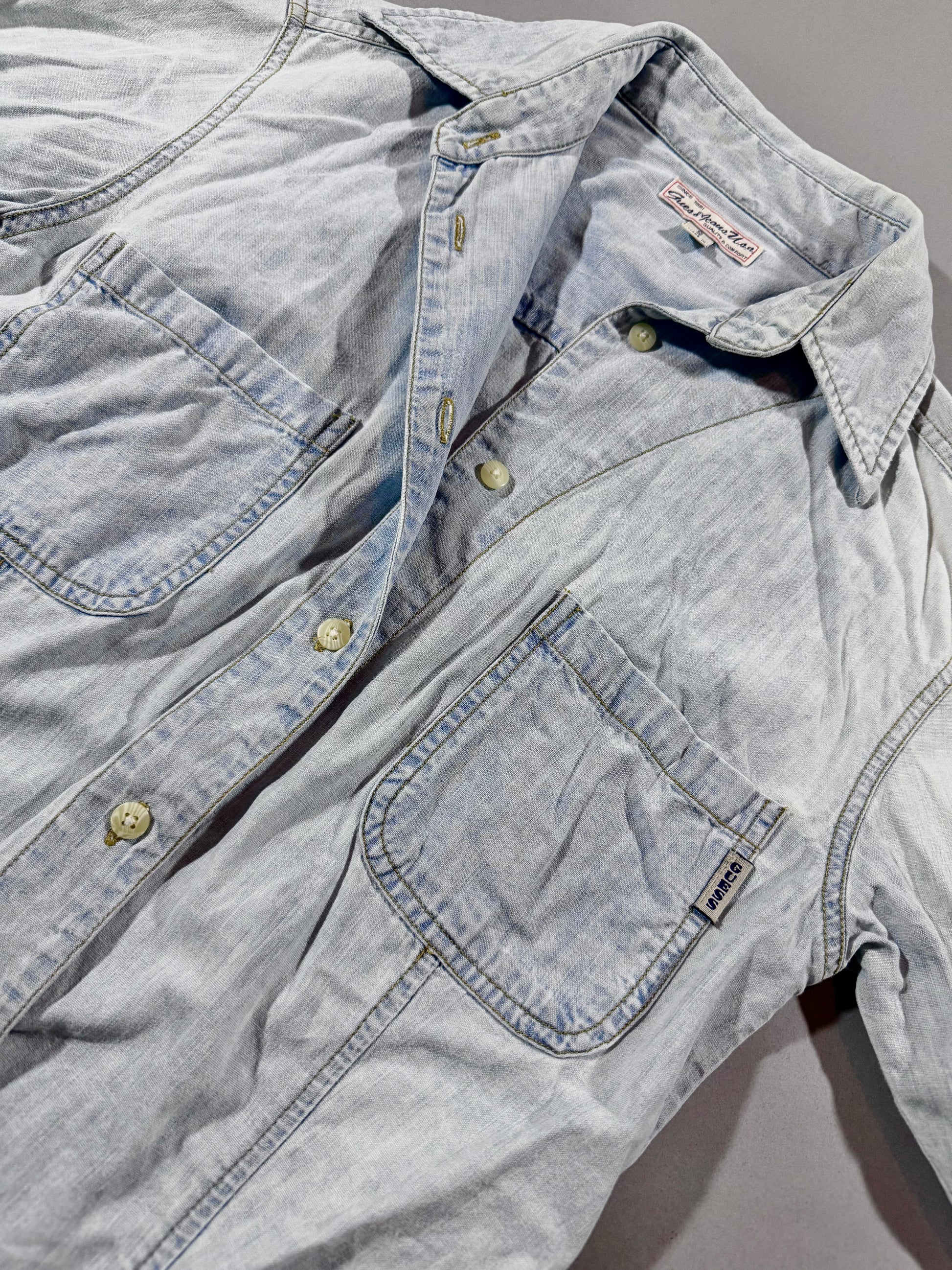 Close-up of vintage Guess Premium Wash chambray denim shirt featuring pointed collar, button front, and chest pockets.