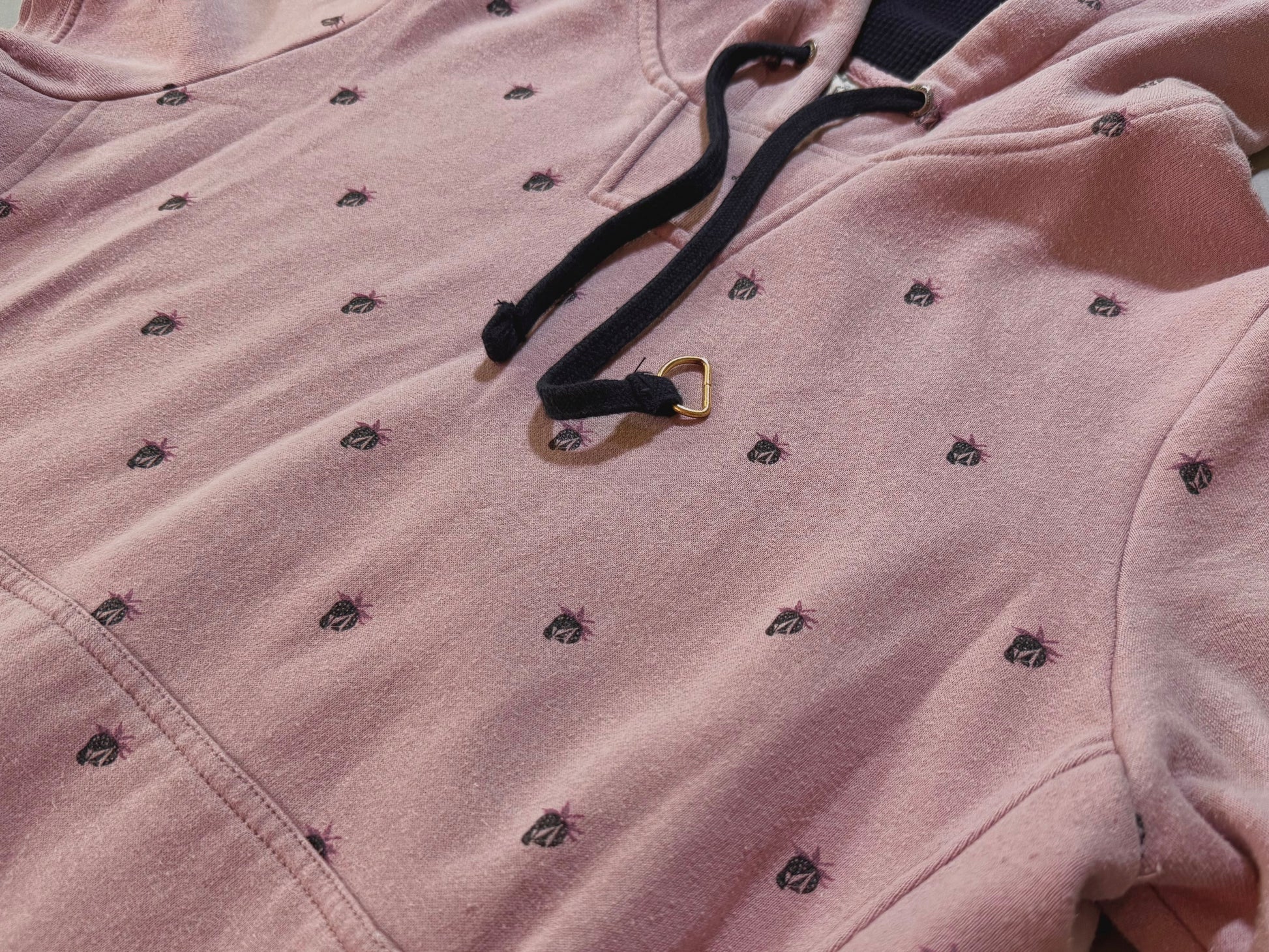 Close-up of vintage Volcom hoodie showing print r Stone/berry pattern, oversized black drawstrings, and soft pink fabric.