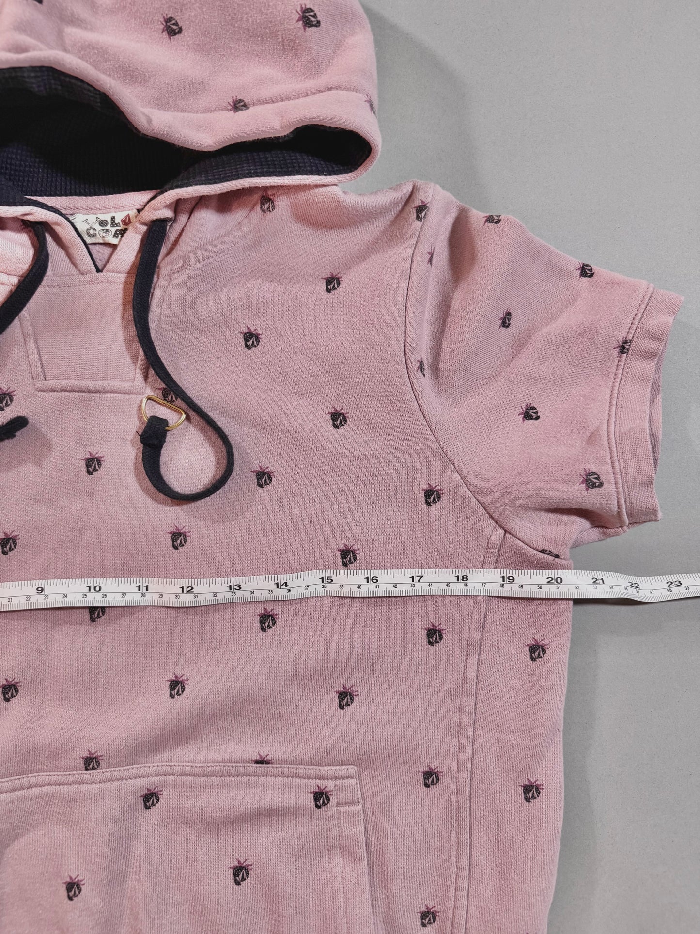 Close-up of vintage Volcom hoodie showing printed Stone logo pattern, oversized black drawstrings, and soft pink fabric.