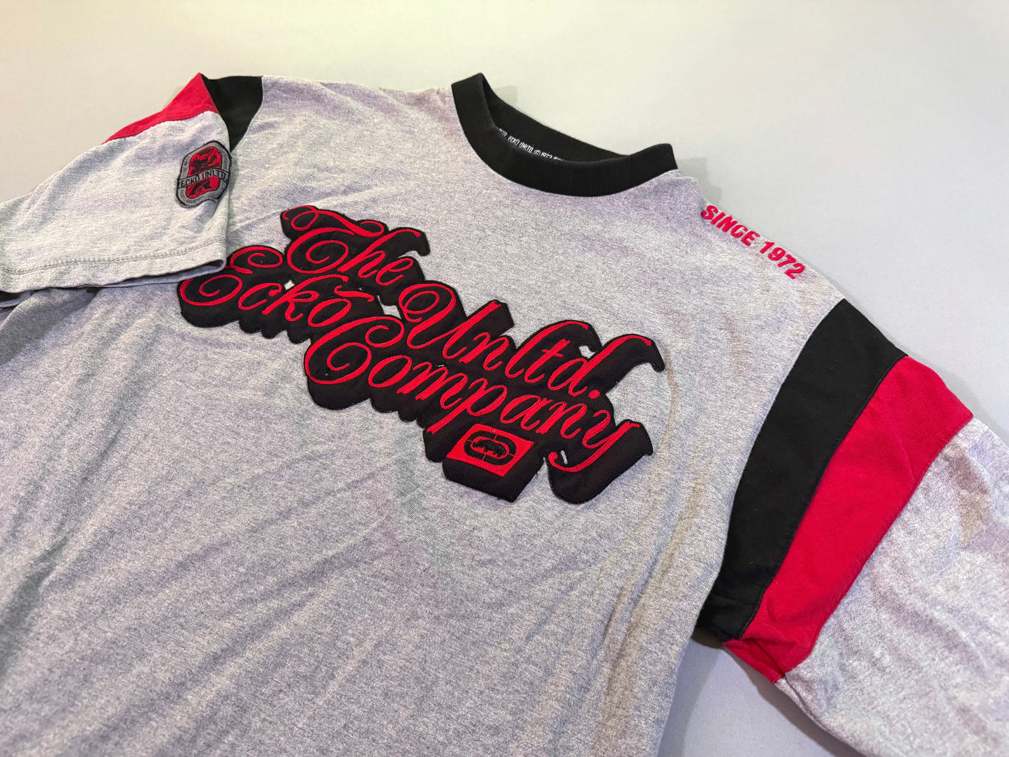 Angled photo of 2000s era Ecko Unltd tee with embroidered cursive branding and colorblock sleeves 
