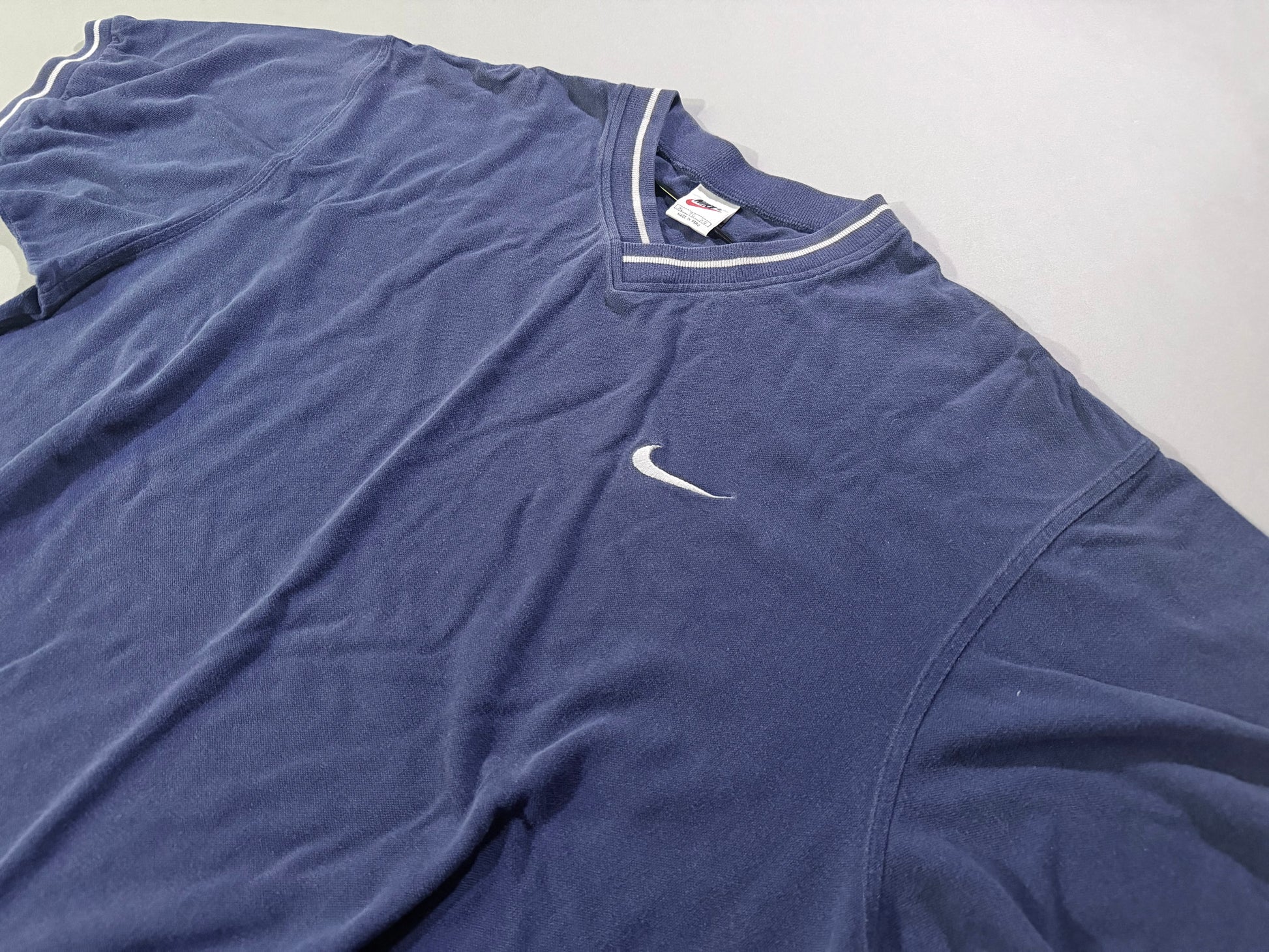 Close angled view of vintage Nike Y2K navy V-neck shirt featuring embroidered white Swoosh and striped collar.