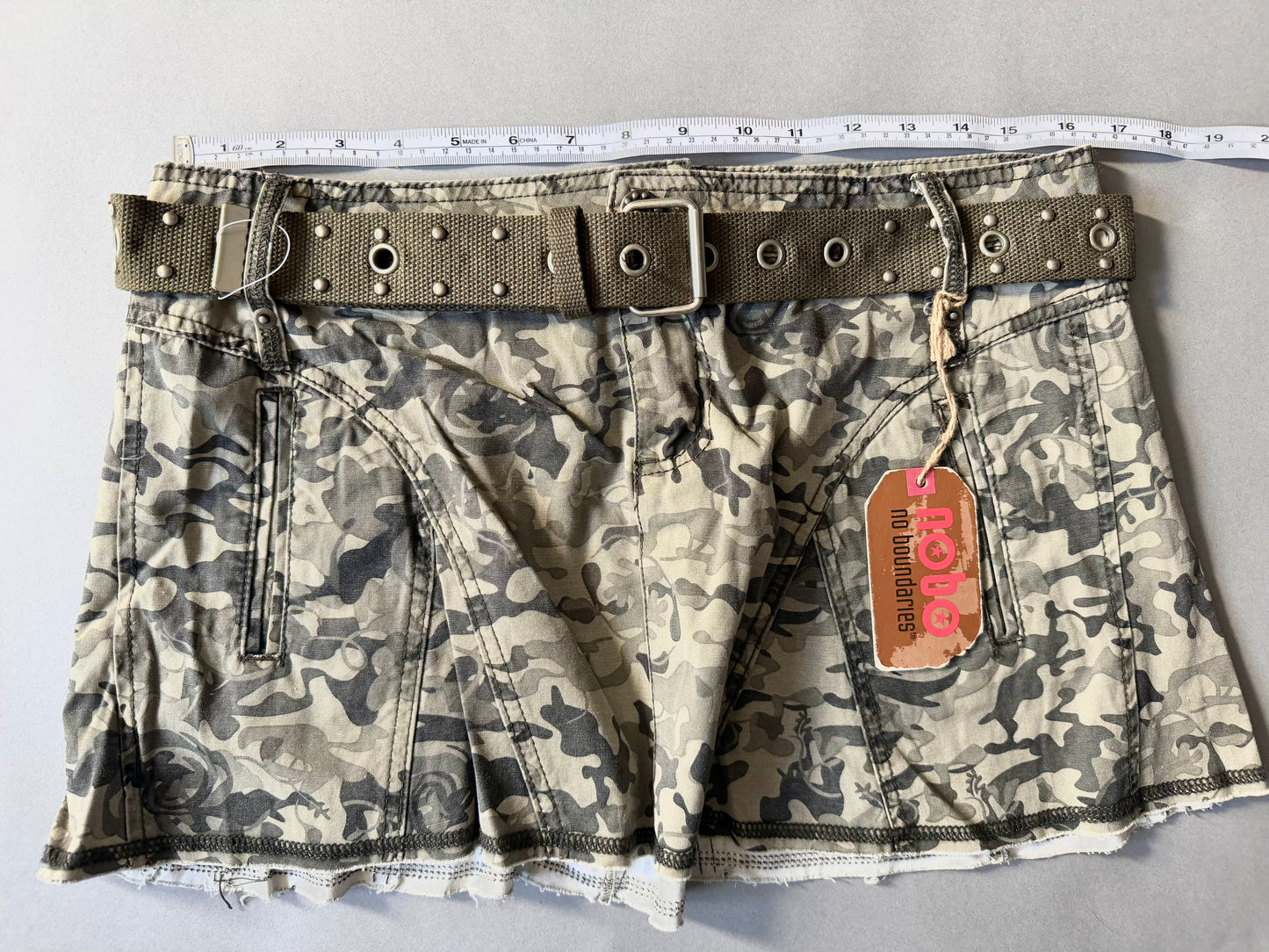 Photo of y2k camo mini skirt with original tags still attached And measuring tape showing 33 inches waist. 