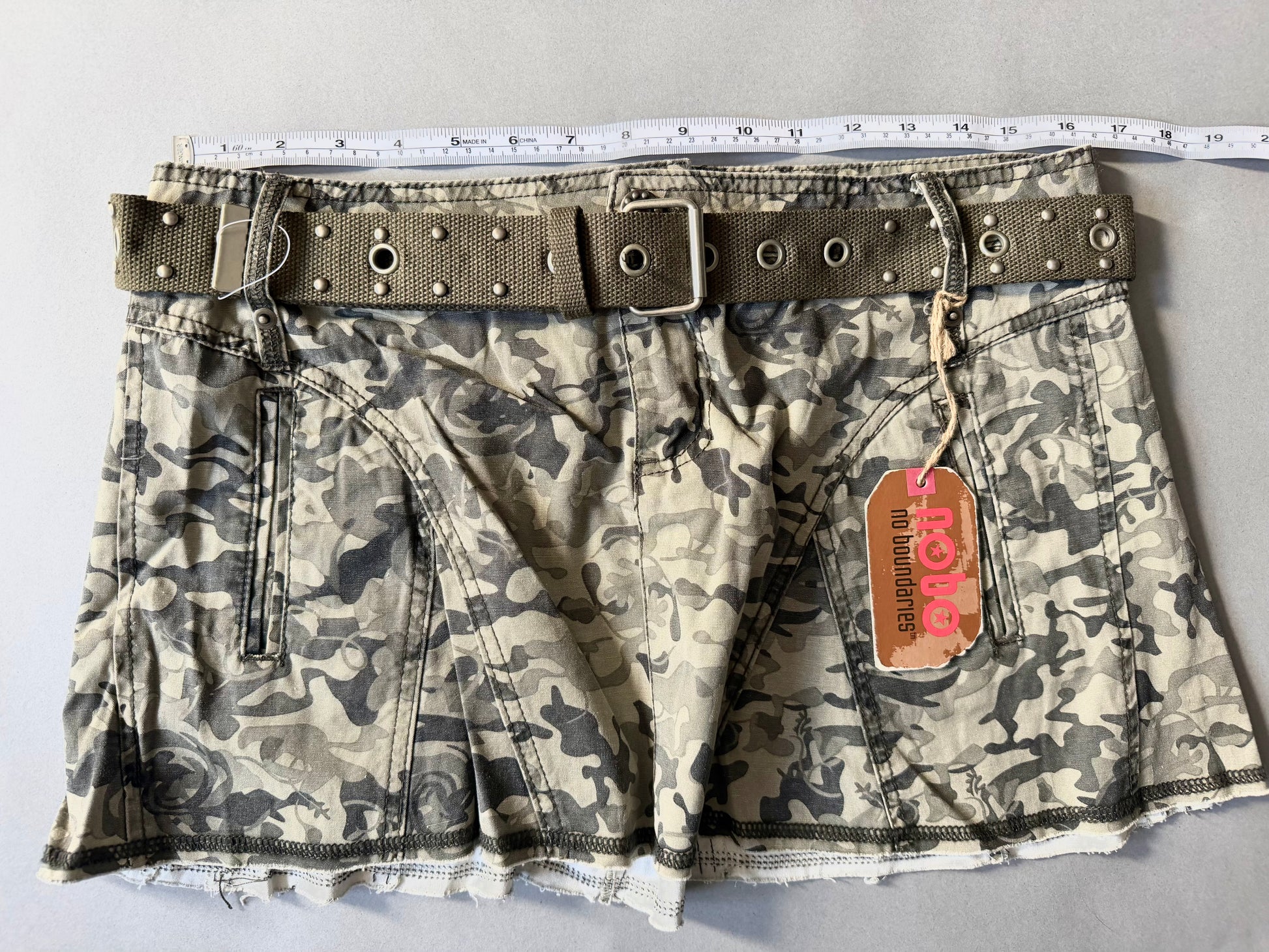 Photo of y2k camo mini skirt with original tags still attached And measuring tape showing 33 inches waist. 