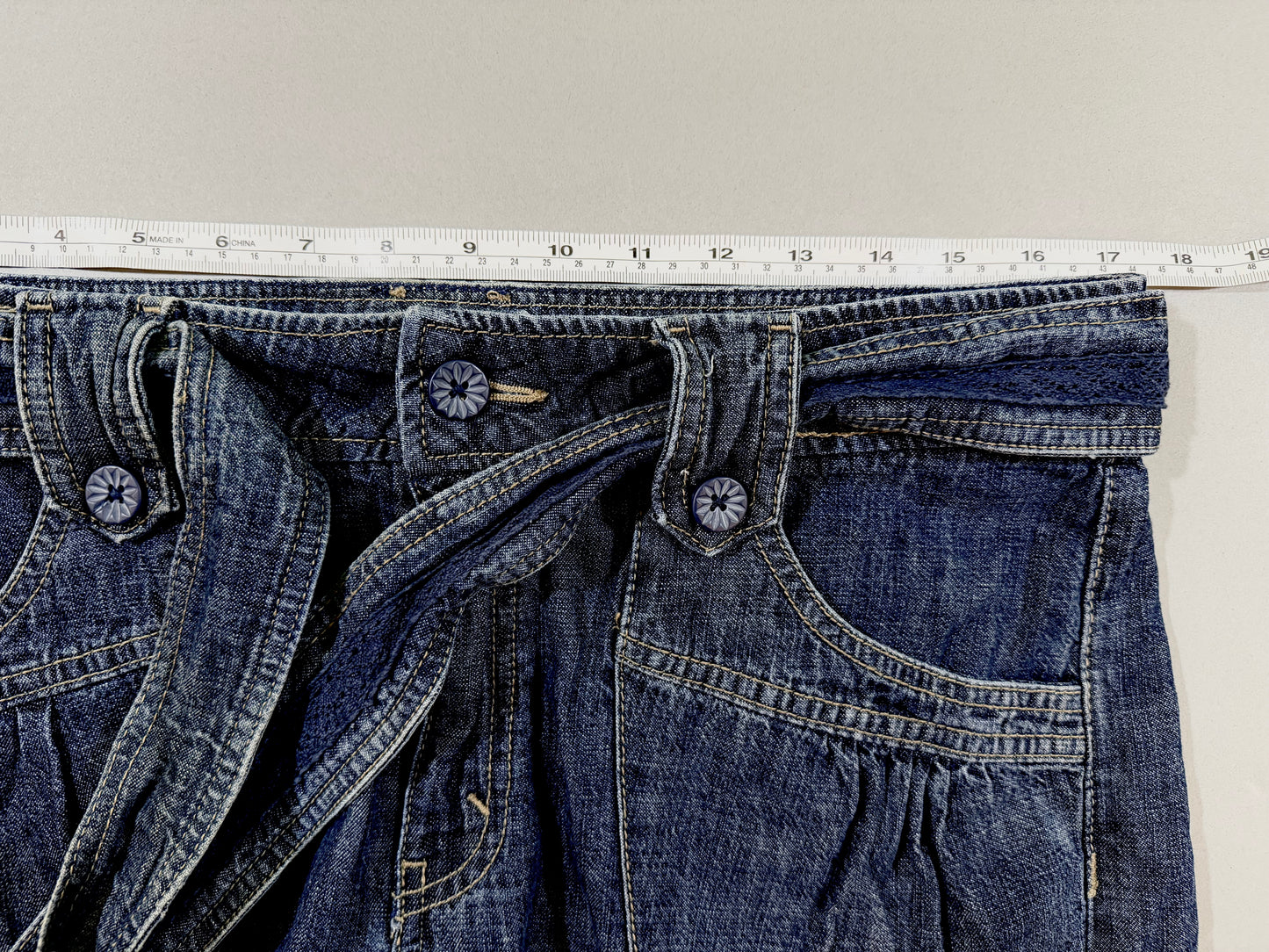 Close-up showing the waistband, decorative buttons, belt loops, and front pocket construction.