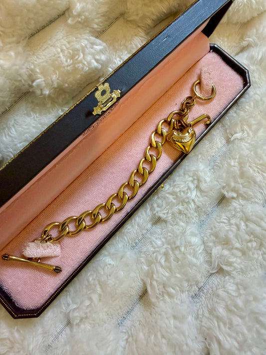 Vintage Juicy Couture gold-tone charm bracelet resting inside its original branded jewelry box with pink velvet lining.