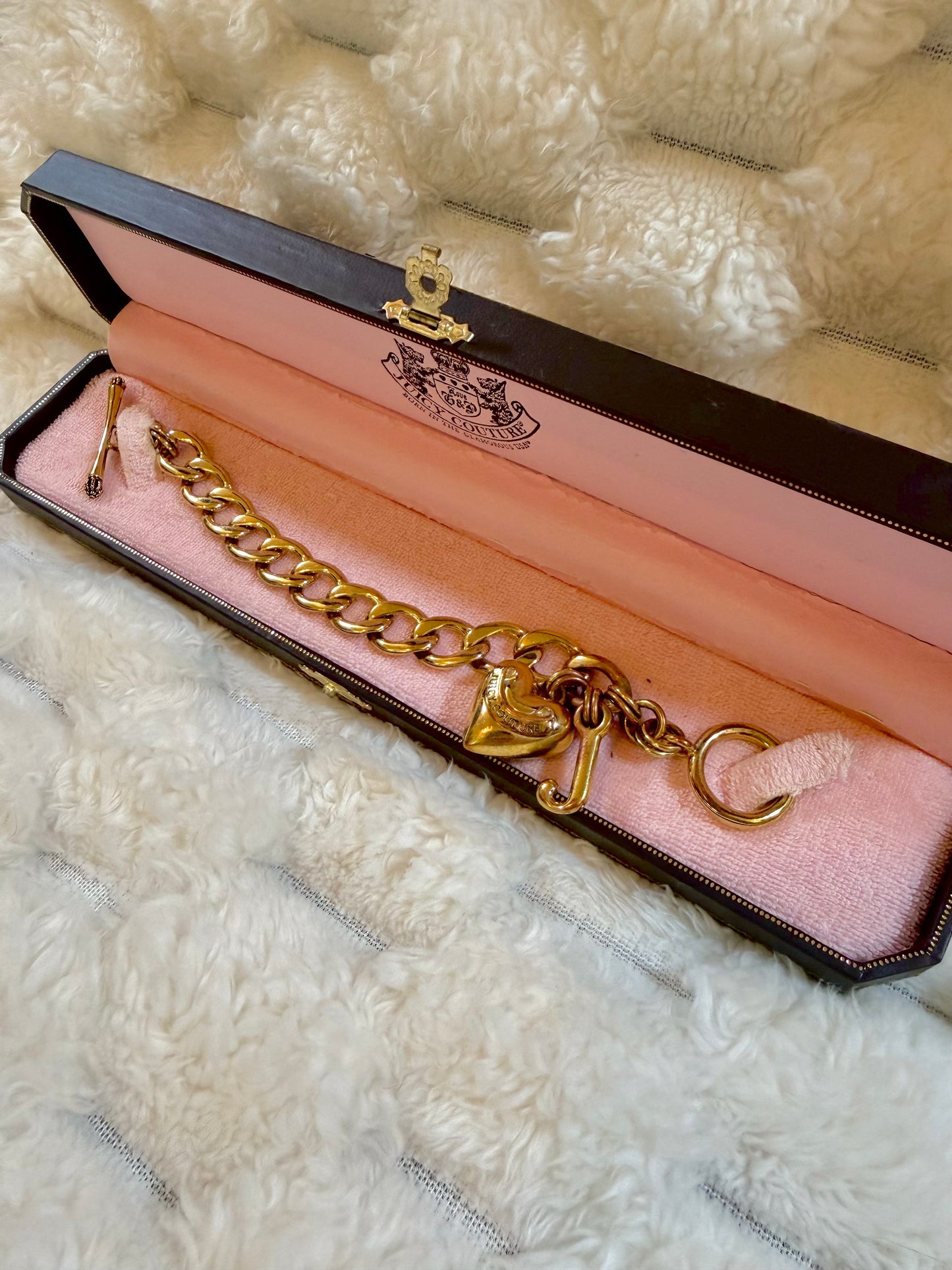 Angled view of an authentic Juicy Couture gold-tone bracelet featuring chunky chain links, heart charm, and original jewelry box.