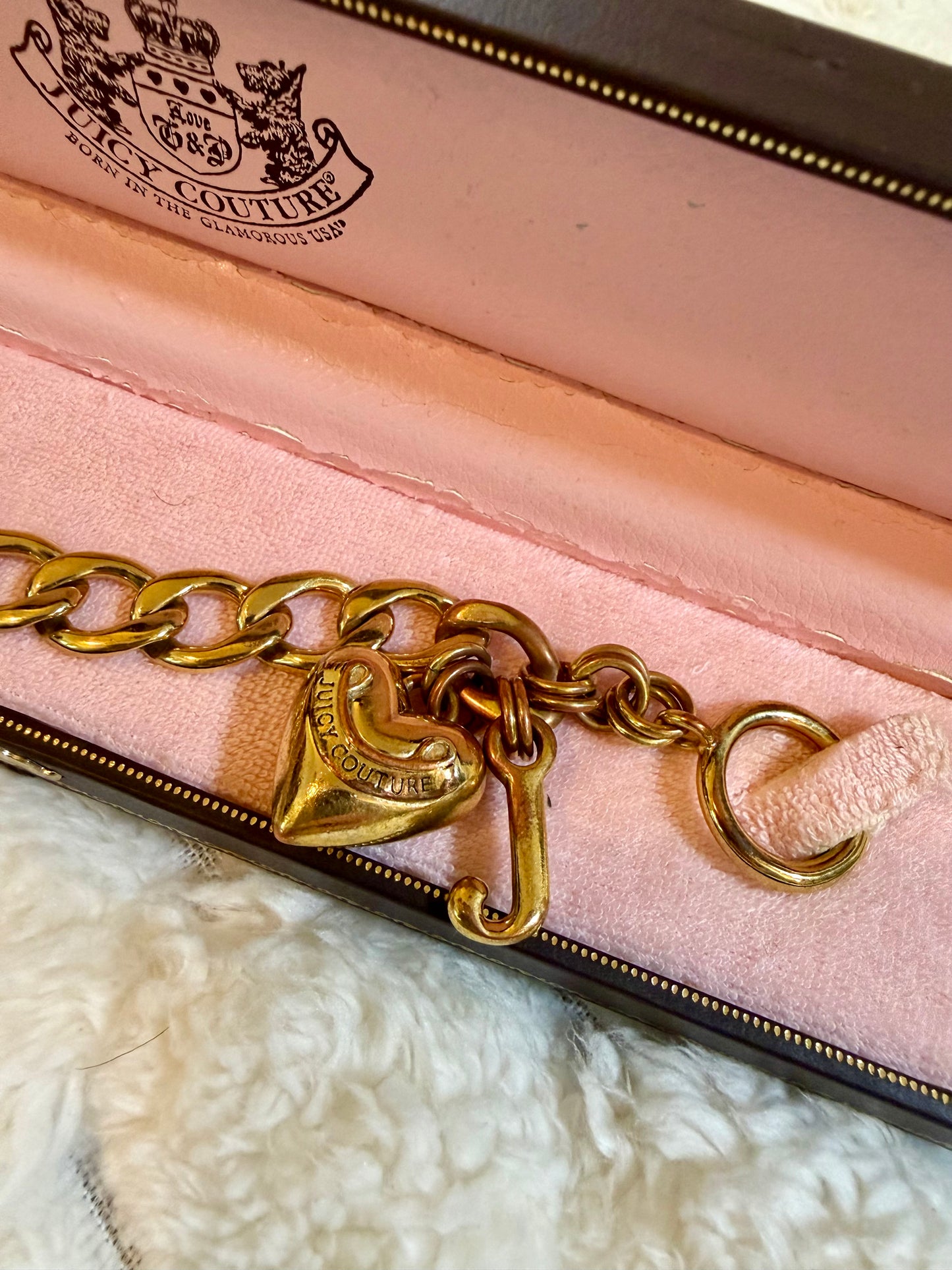 Juicy Couture gold-tone charm bracelet with signature heart and J charms displayed inside the original pink velvet presentation box.